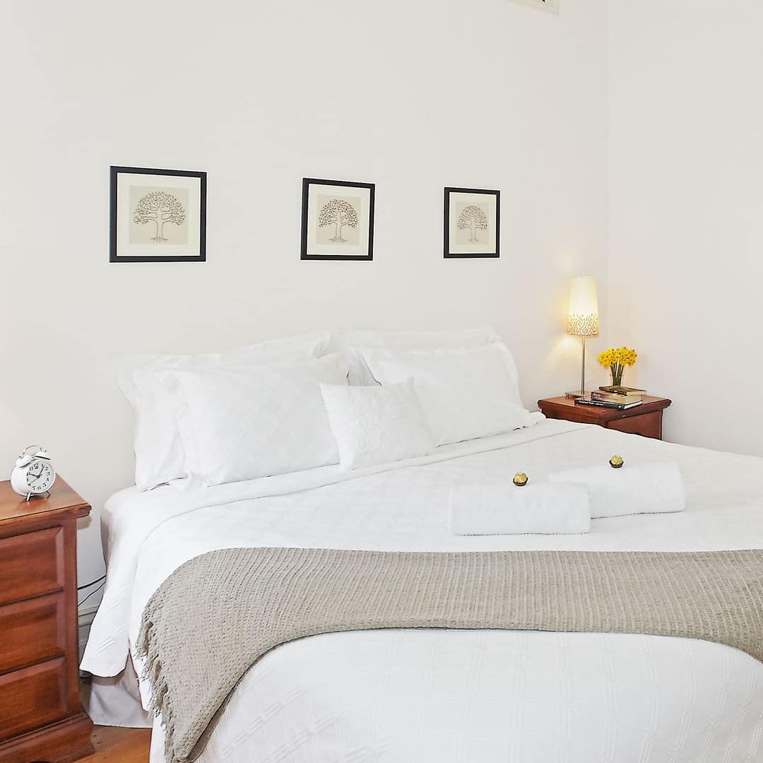 Bright bedroom with hardwood floors, a king size bed, white bedding, wooden bedside tables, towels and chocolate on bed.