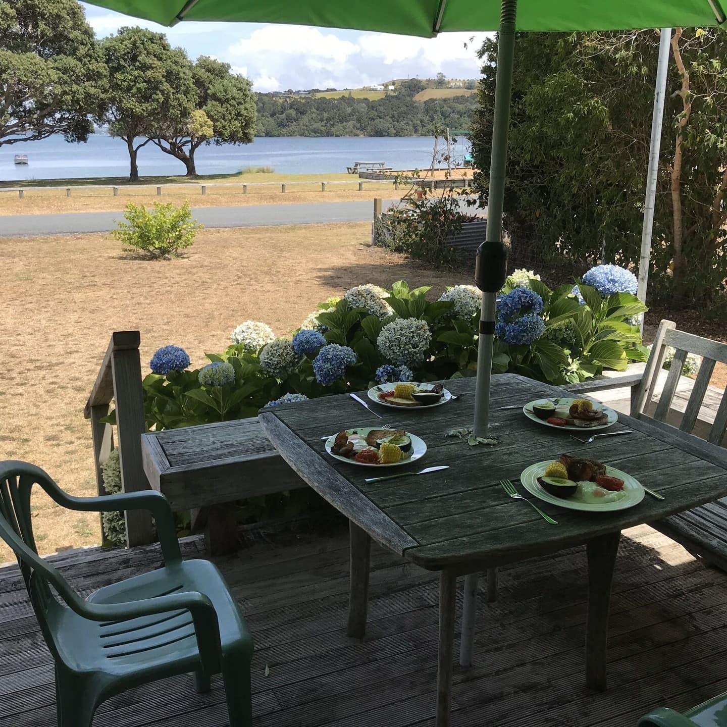 Dinner set for 4 on the back wooden deck of a beachfront bach under an umbrella
