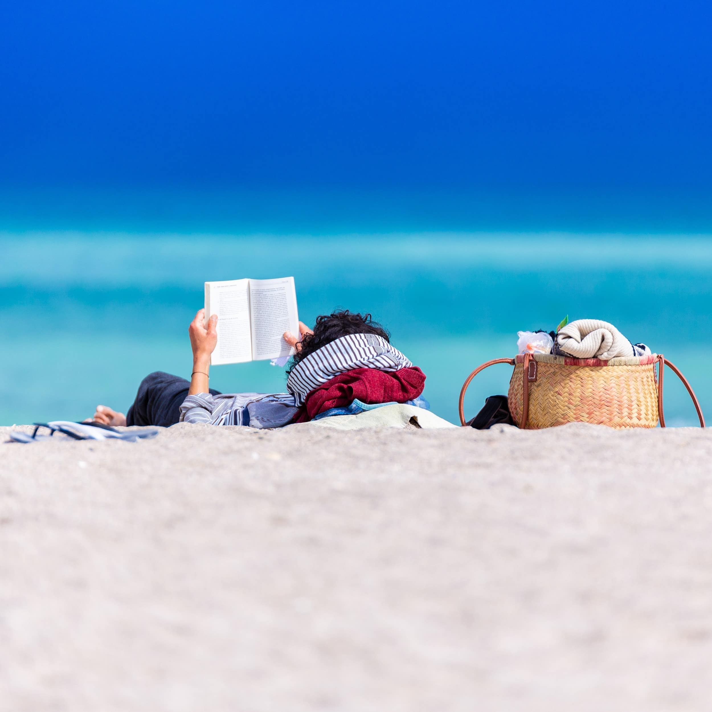Person lying down on the beach relaxing and reading a book