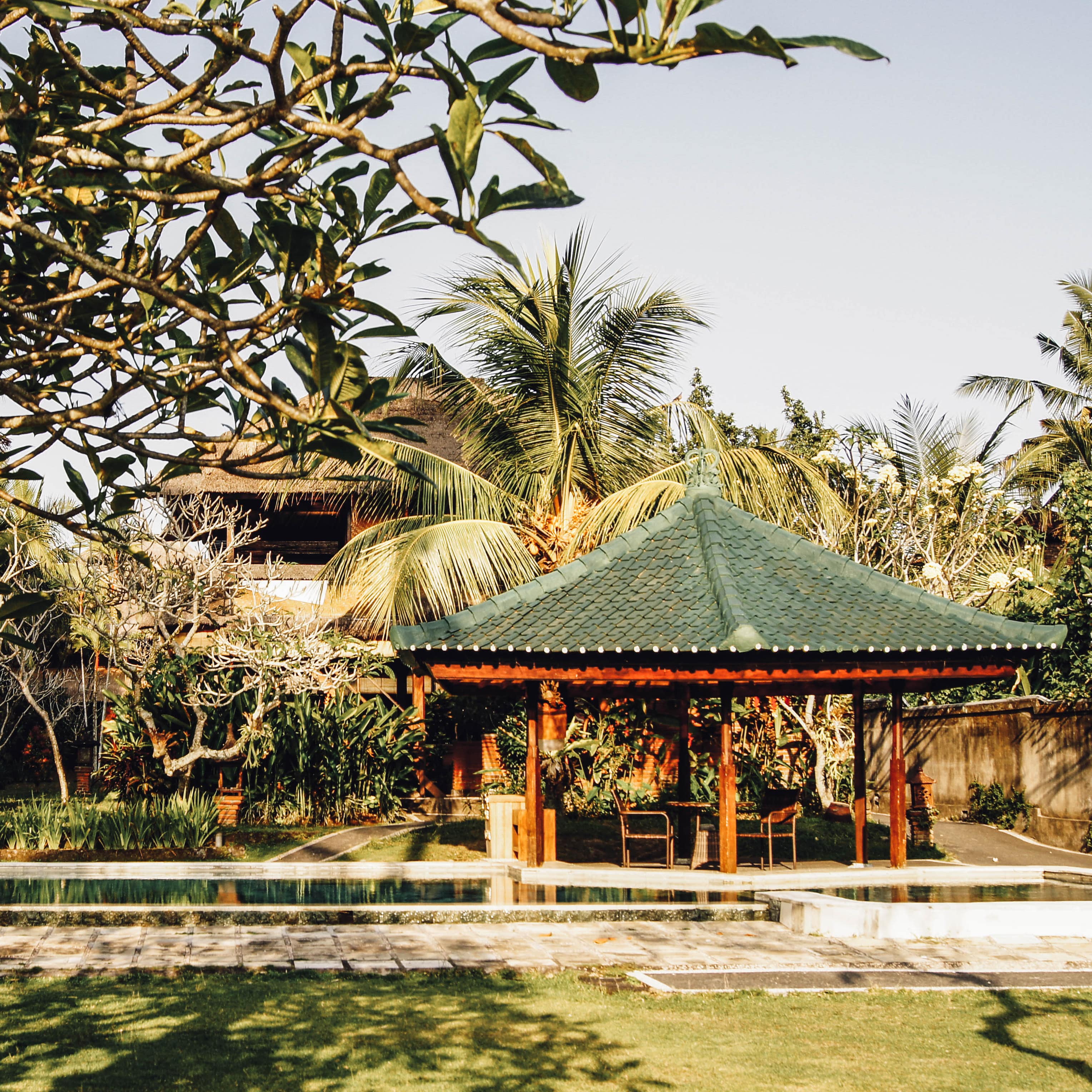 Rectangular private pool of villa with a green tile pavilion and al fresco dining with palms and tropical trees