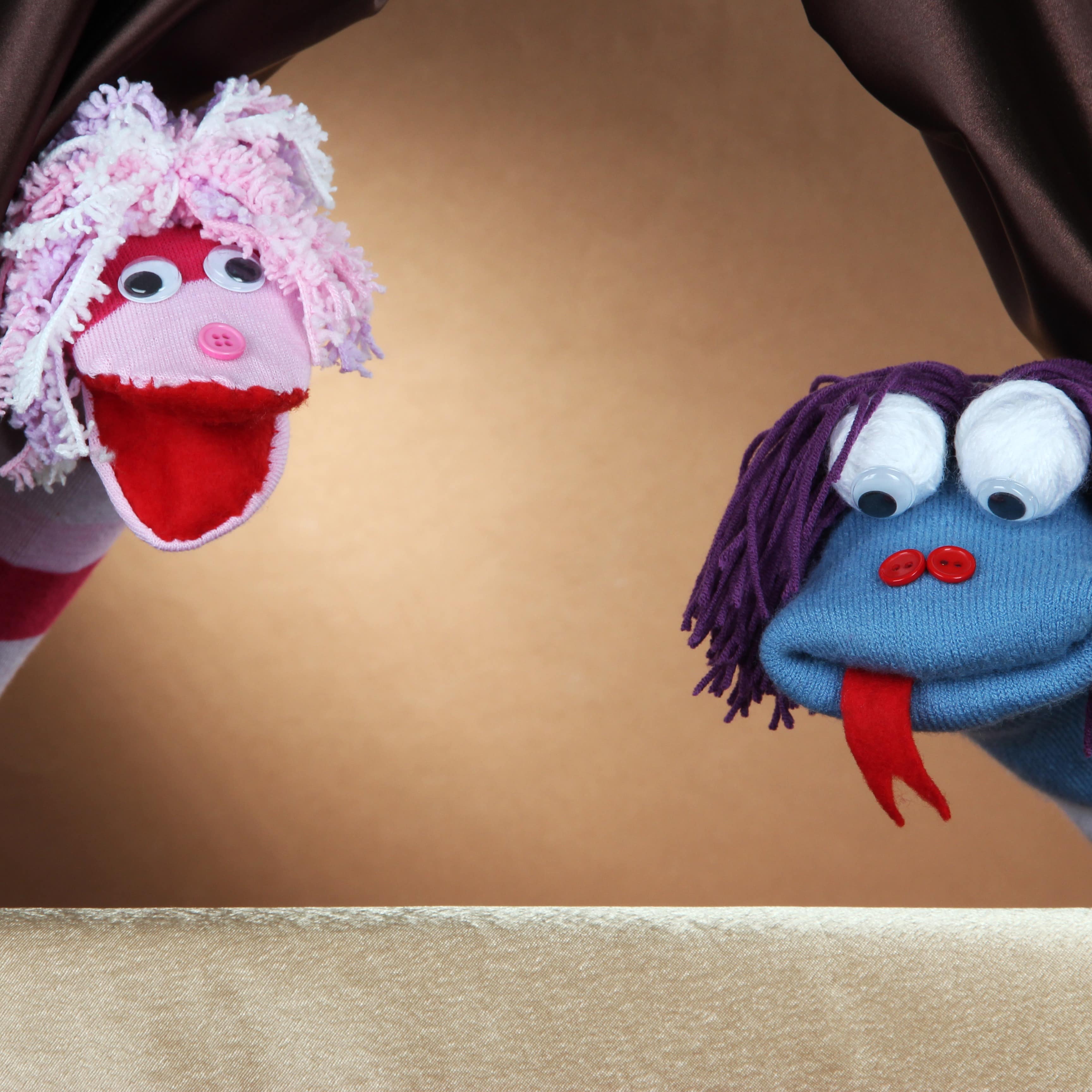 Two hand puppets peeking out of curtain at audience