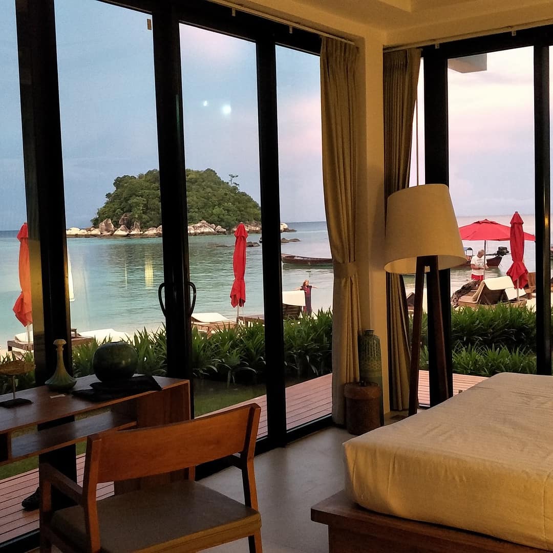 Bedroom of waterfront Thai villa with floor-to-ceiling windows, a desk and chair and a view of the water and a small island