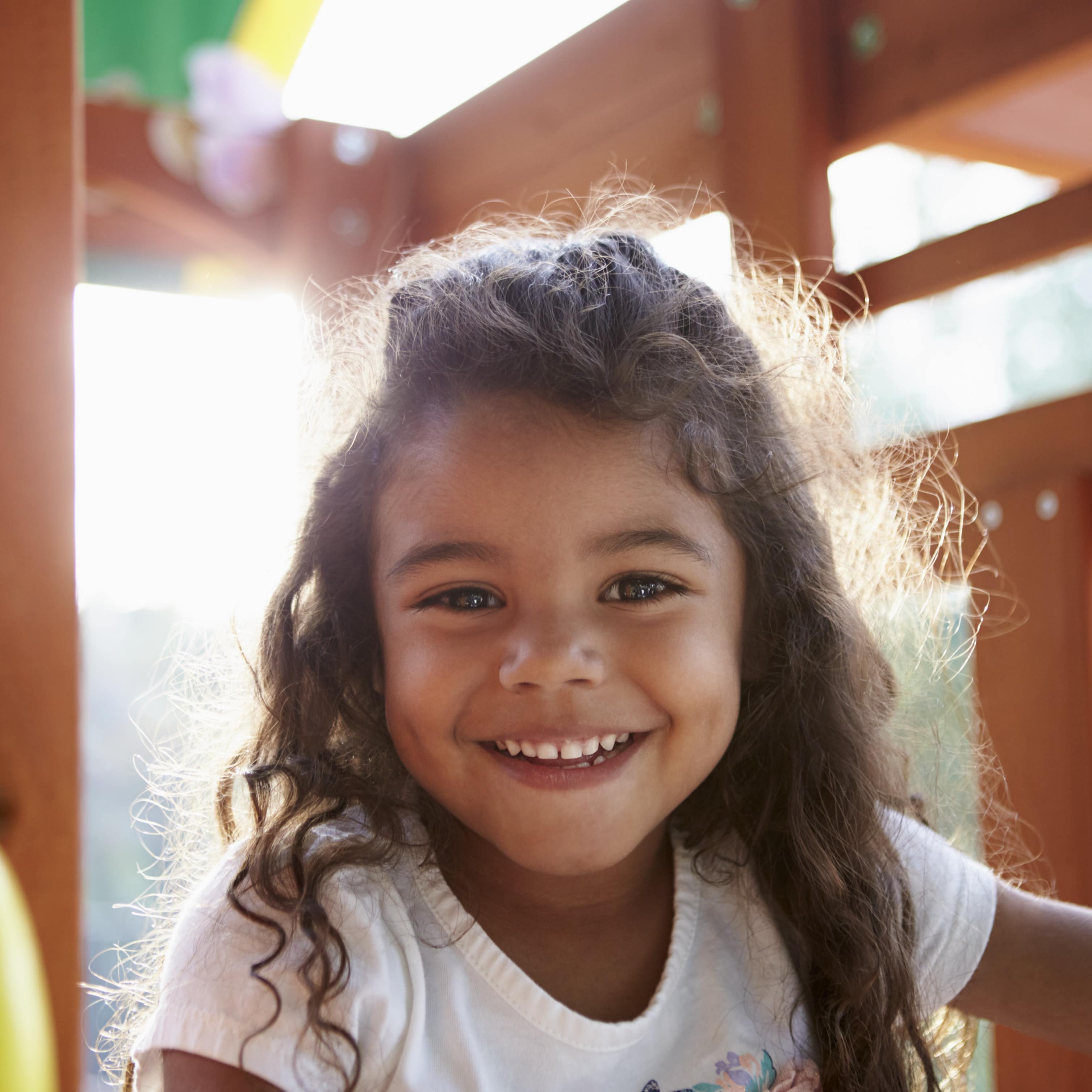 Smiling girl playing on a climbing frame in a playground up close