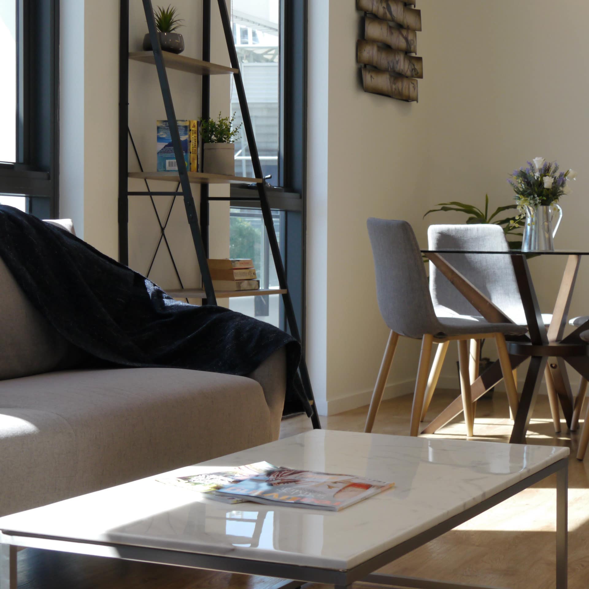 Open living and dining area with beige cloth sofa, blue chair, marble-top coffee table and wood and glass dining table