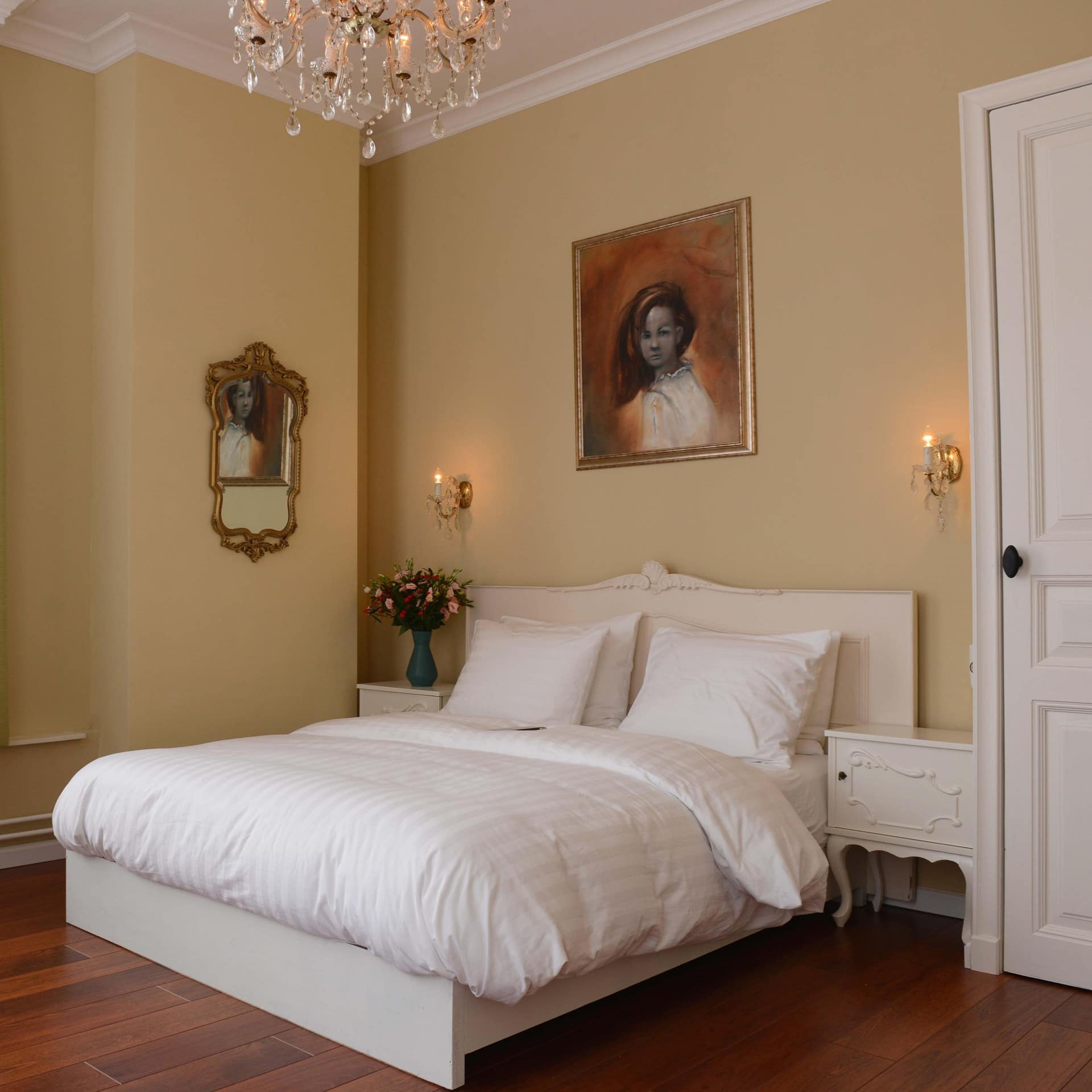 Spacious bedroom with hardwood floors, light yellow walls, a king size bed with white bedding, and antique furniture.