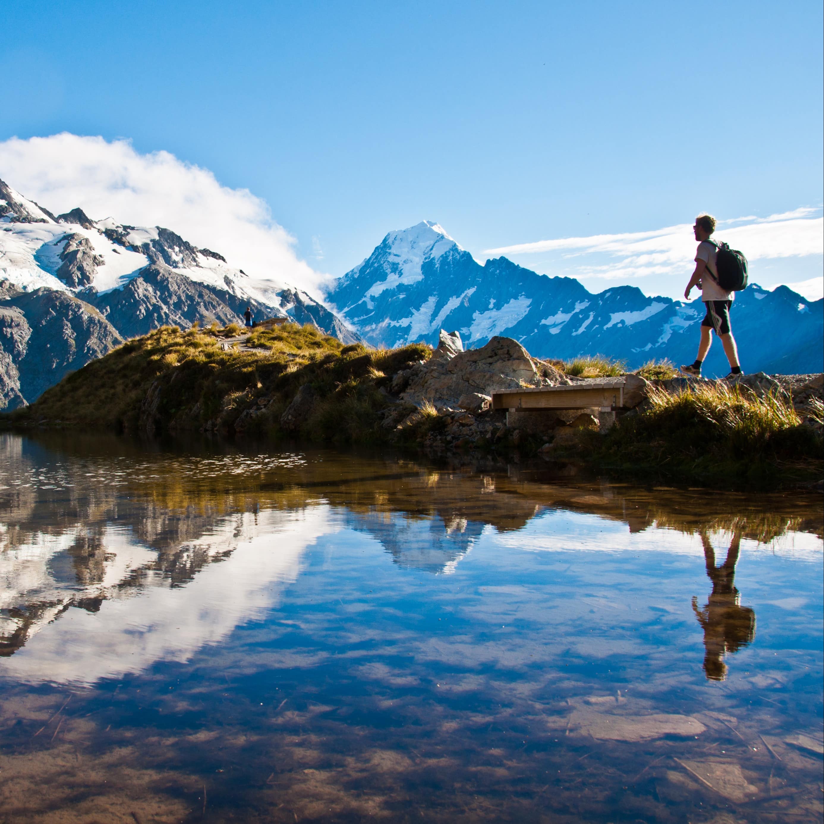 Man hiking around Lake Pukaki with Mount Cook in the background reflected by the lake water