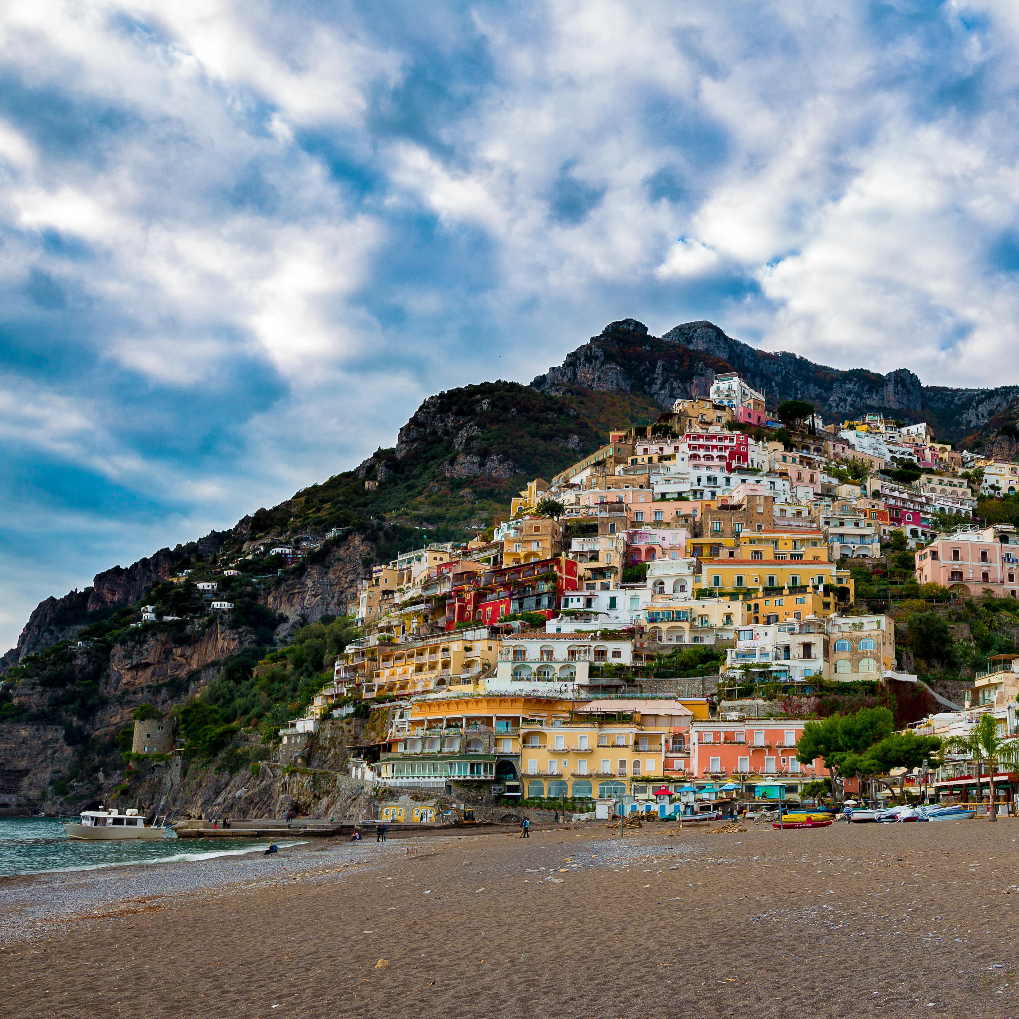 A view of Positano from the beach with colourful villas stretching up the hillside against verdant cliffs