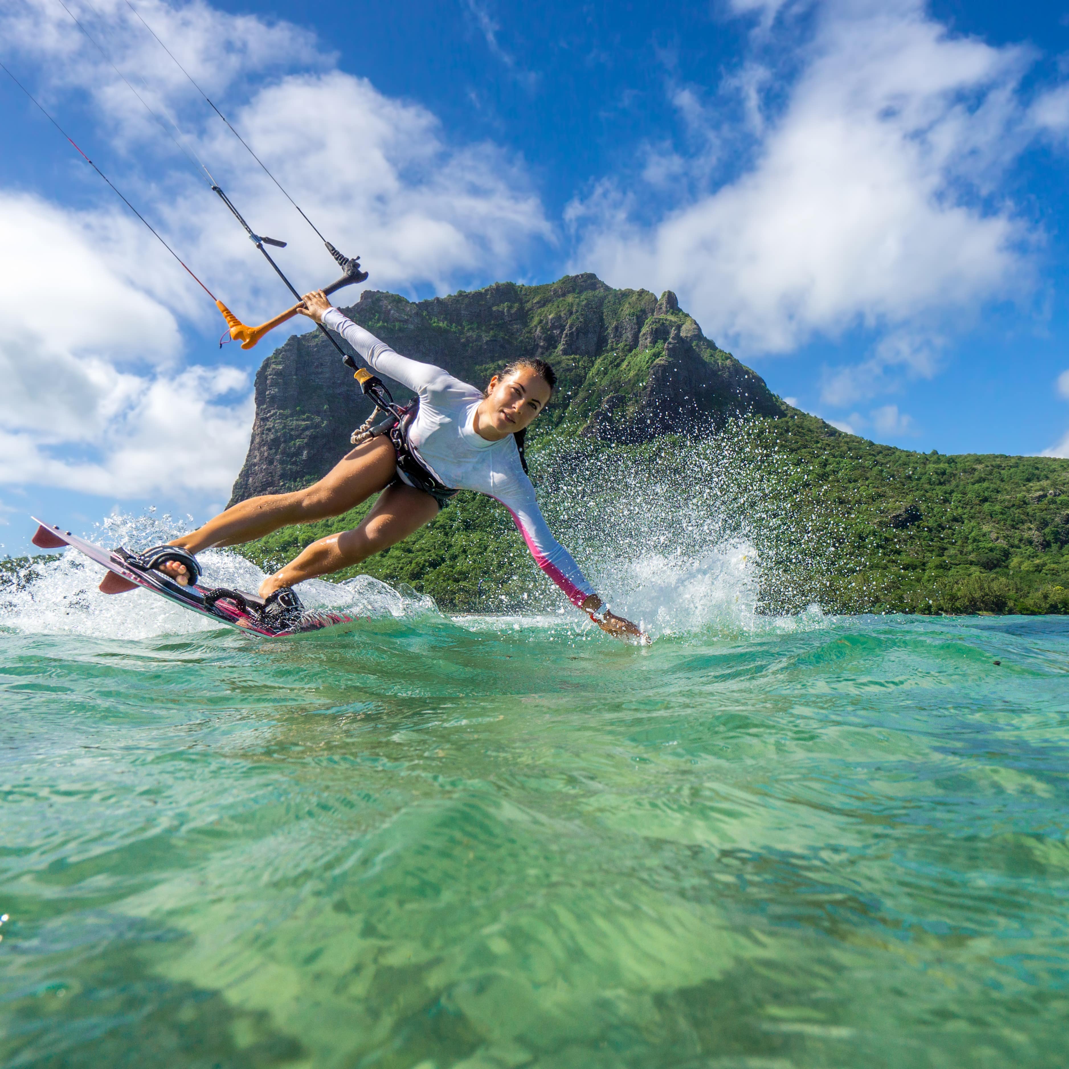 Woman kitesurfing off the coast with a mountain in the background