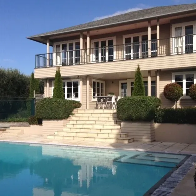 Back of cream-coloured 2-storey house with steps leading down from the porch to a pool