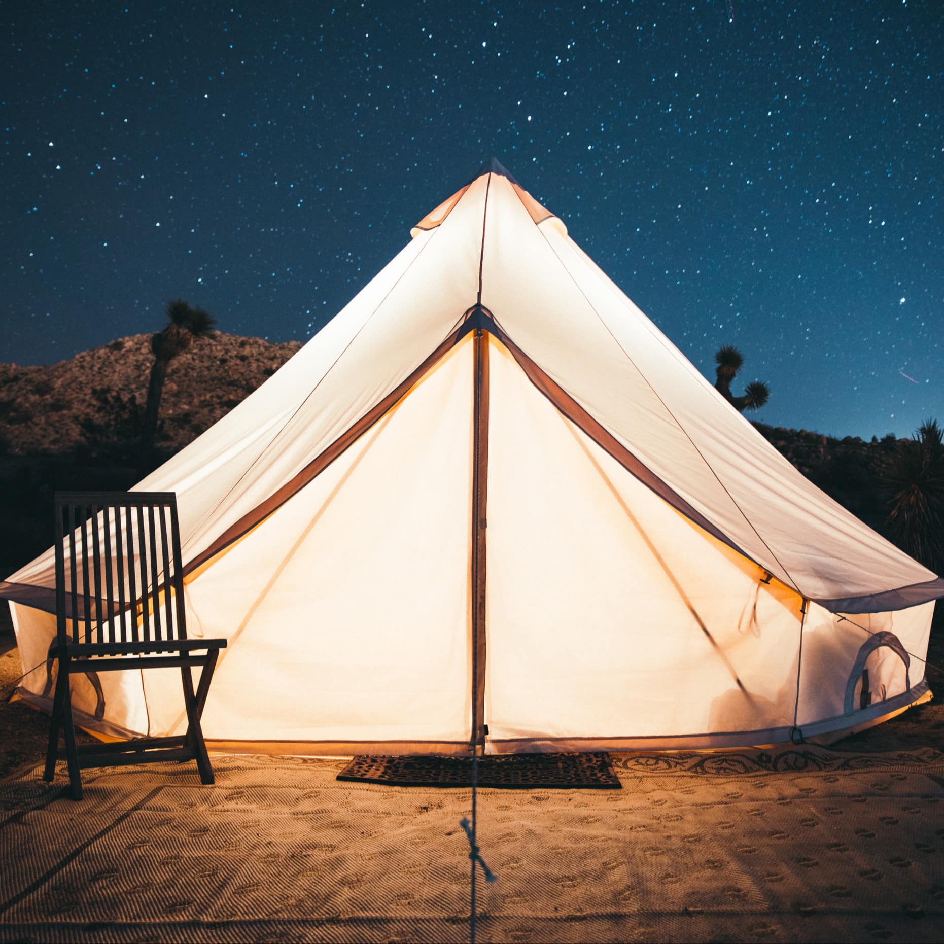 Campsite with a luxury tent under shooting stars in the bush with a wooden folding chair and a rug