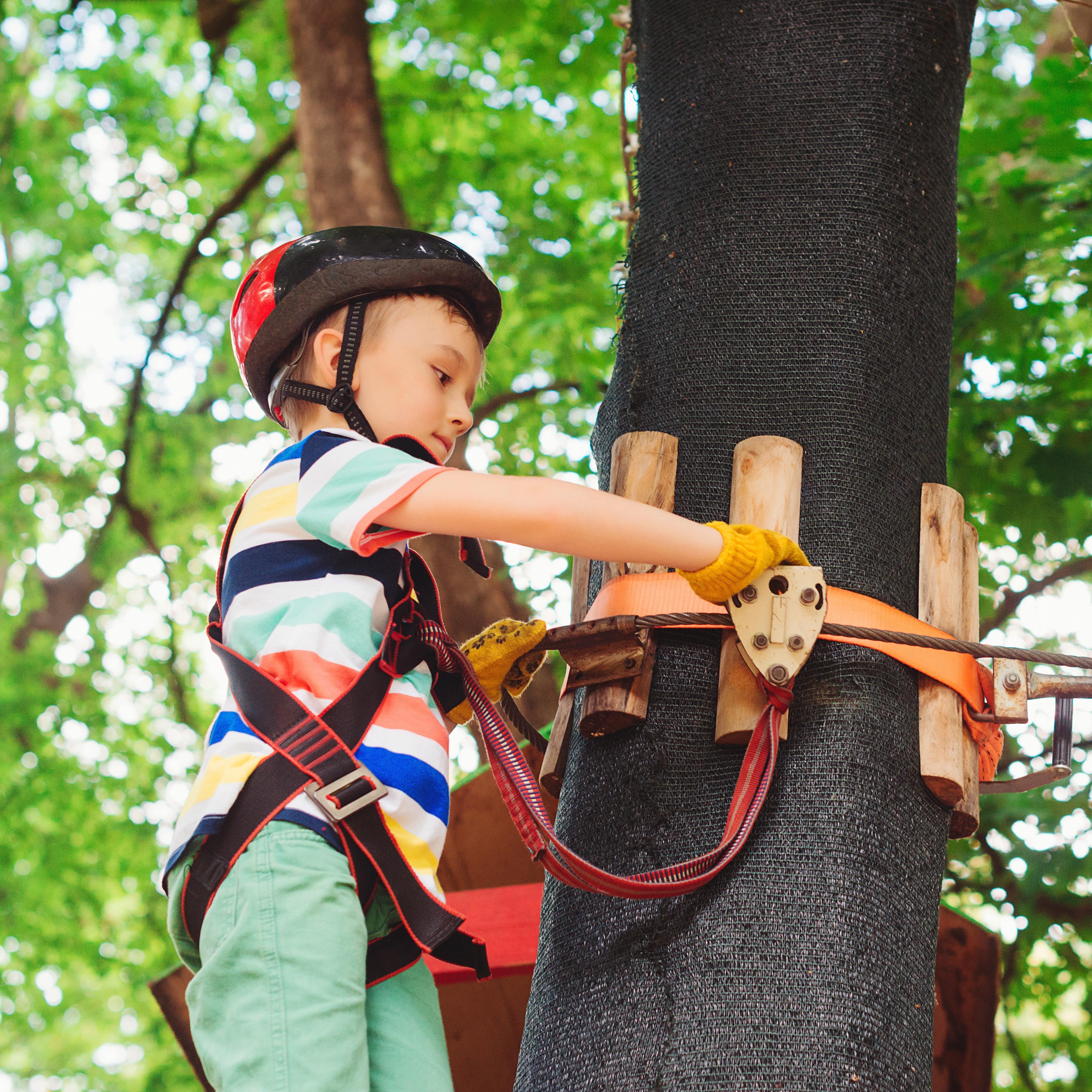 Young boy with helmet hooks to rope and stands on a platform ready to start treetop adventure