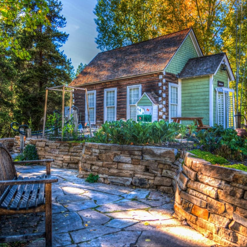 Farm house made with logs and shake siding set against woodland with landscaped stone garden and garden bench