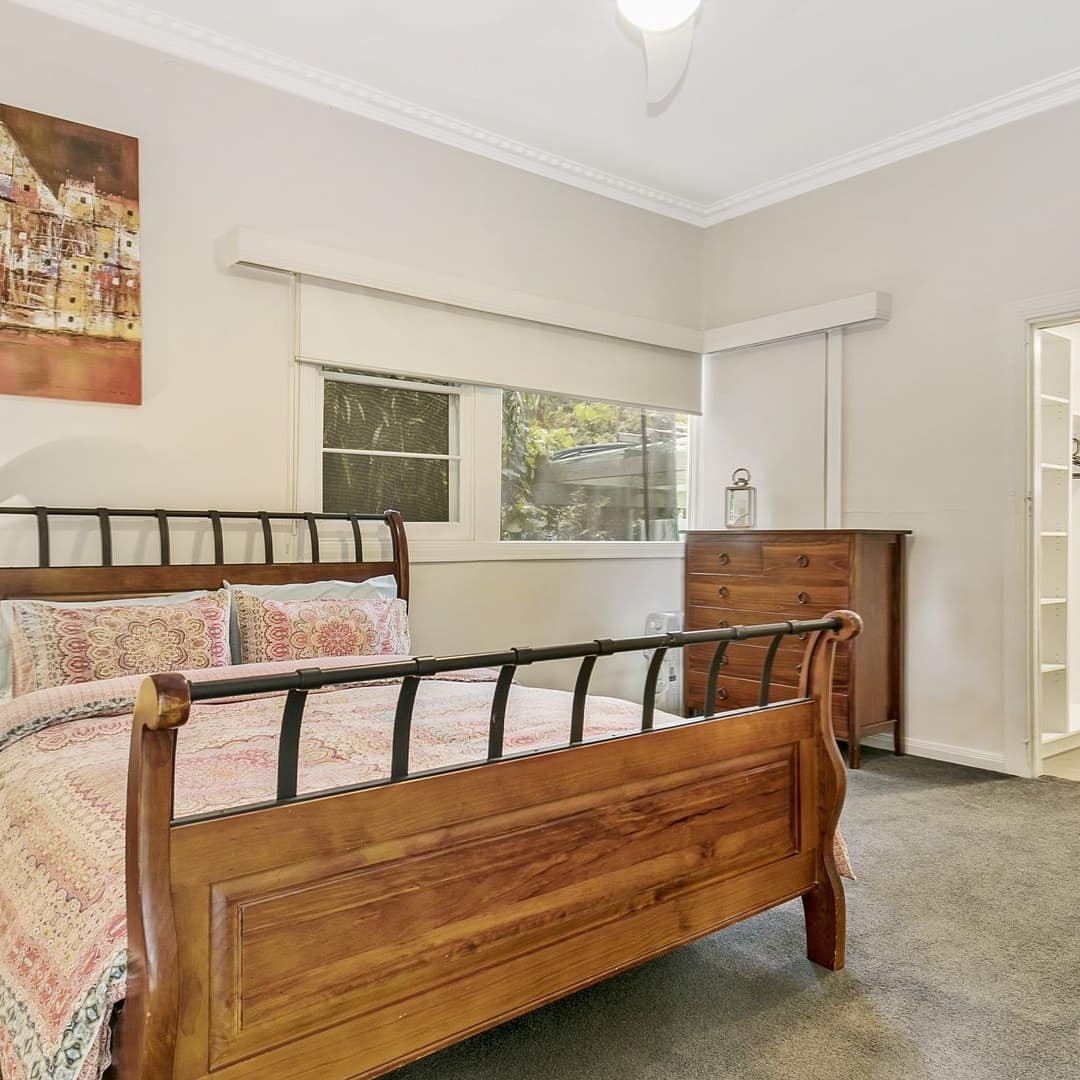 Spacious bedroom with grey carpet, white walls, a wood-framed queen bed, floral bedding, and attached bathroom.