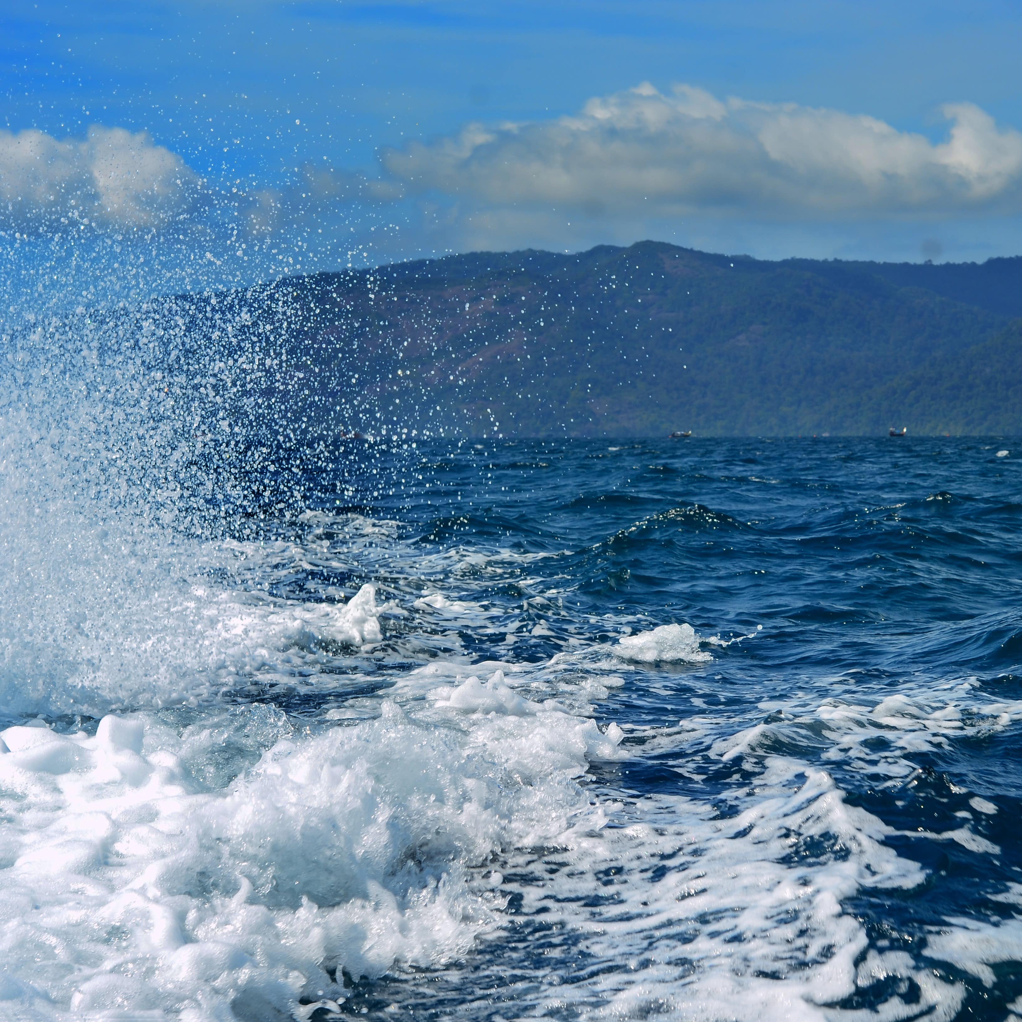 Water spray from speedy watercraft with blue sky and mountains in background
