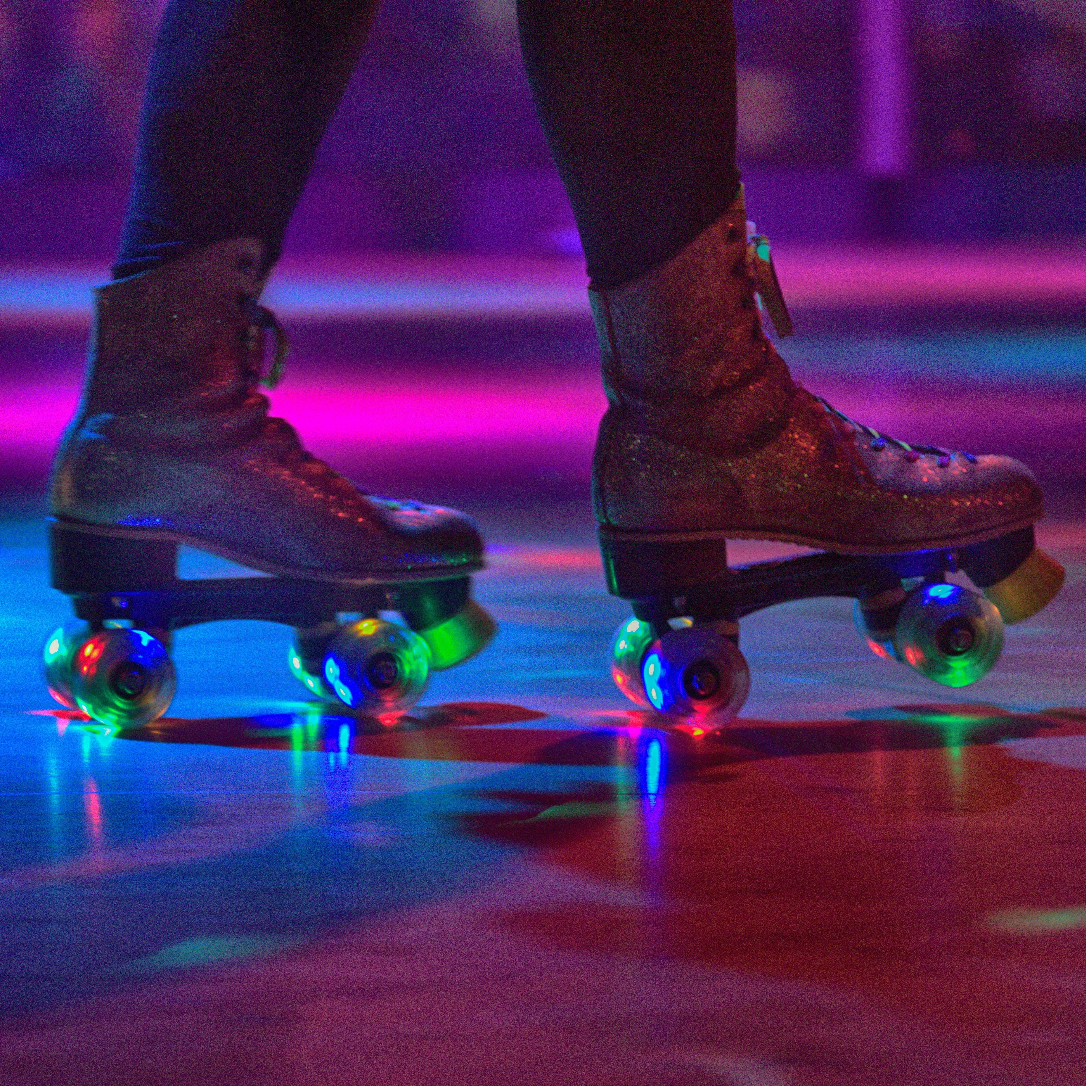 Feet of a person wearing roller skates on dark lit rink
