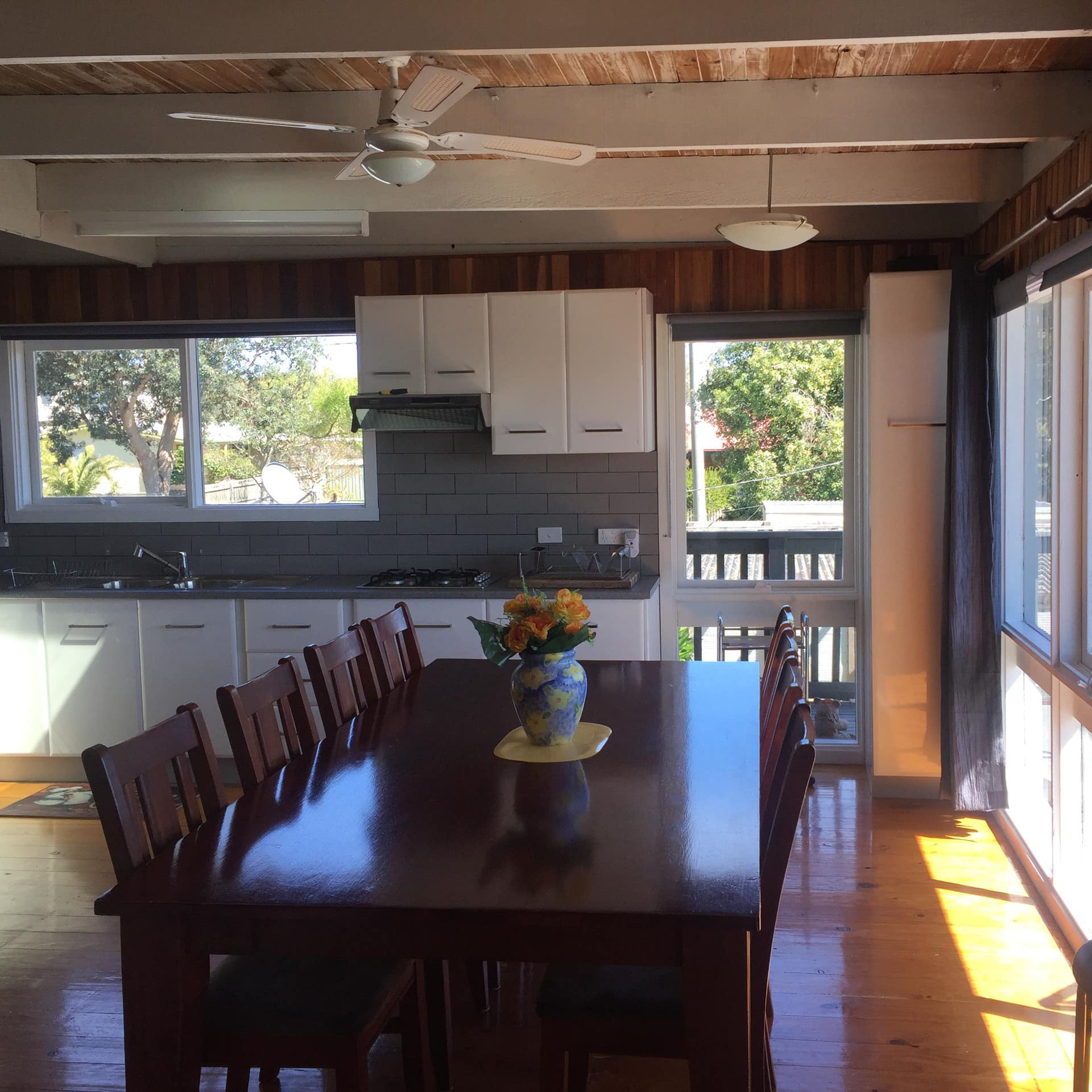 Open dining room and kitchen with hardwood floors, wooden dining table, white cabinets and tall windows.
