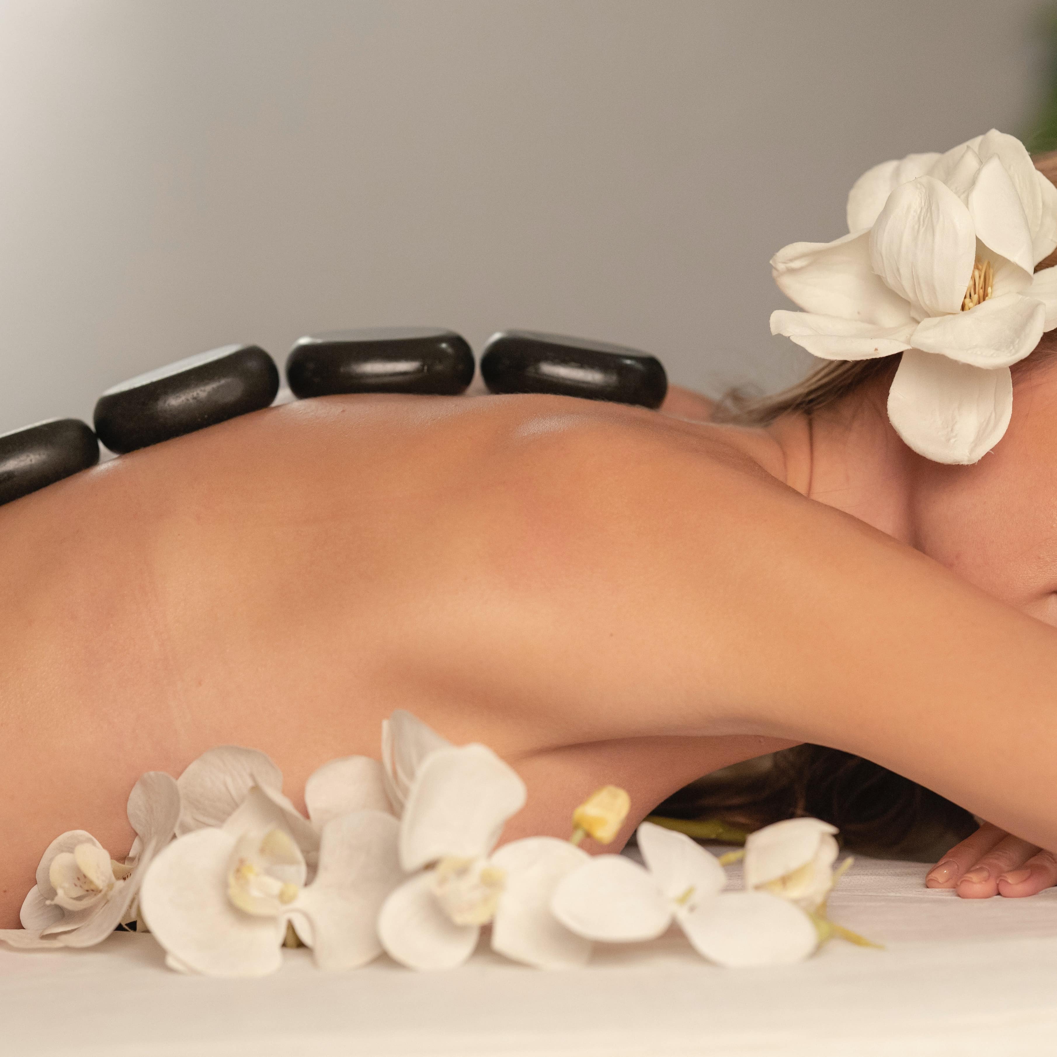 A woman getting a hot stone massage with flowers in her hair