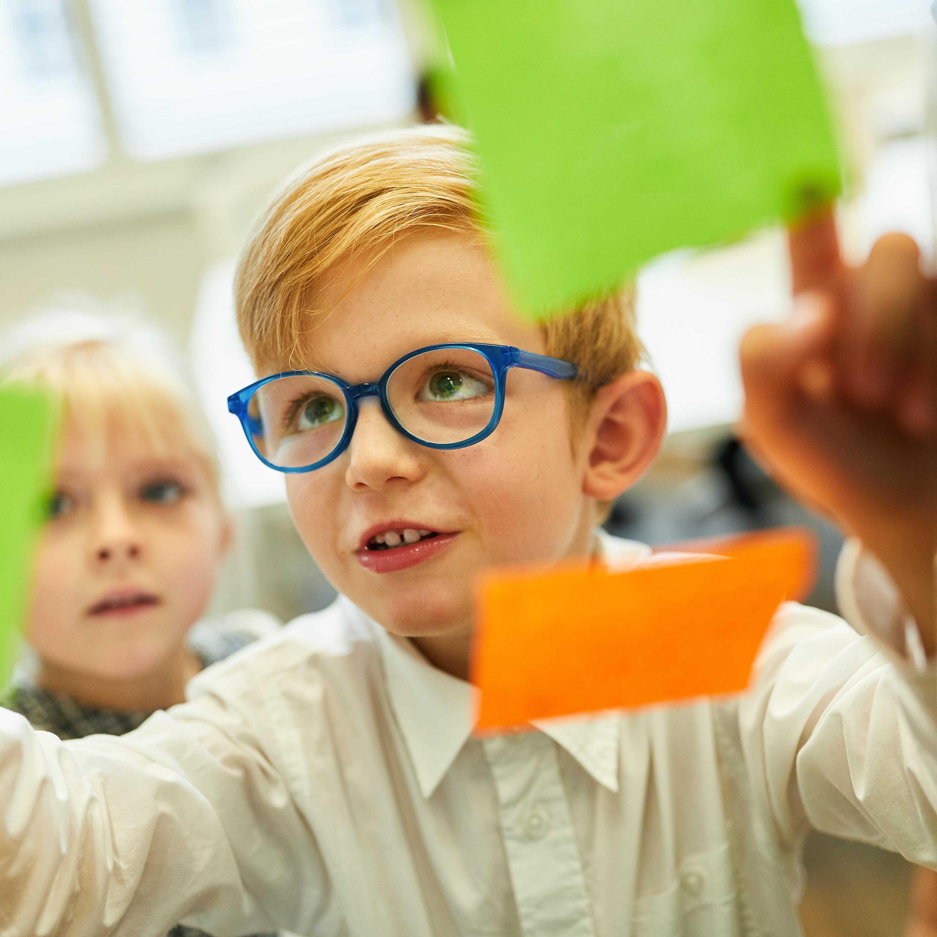 Young boy with blue glasses in a science museum writing and posting sticky notes in a workshop