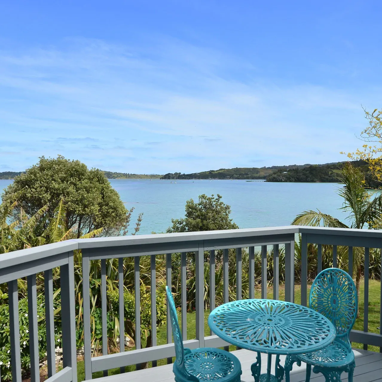 Balcony of a beach home with a small blue garden table and chairs overlooking the bay