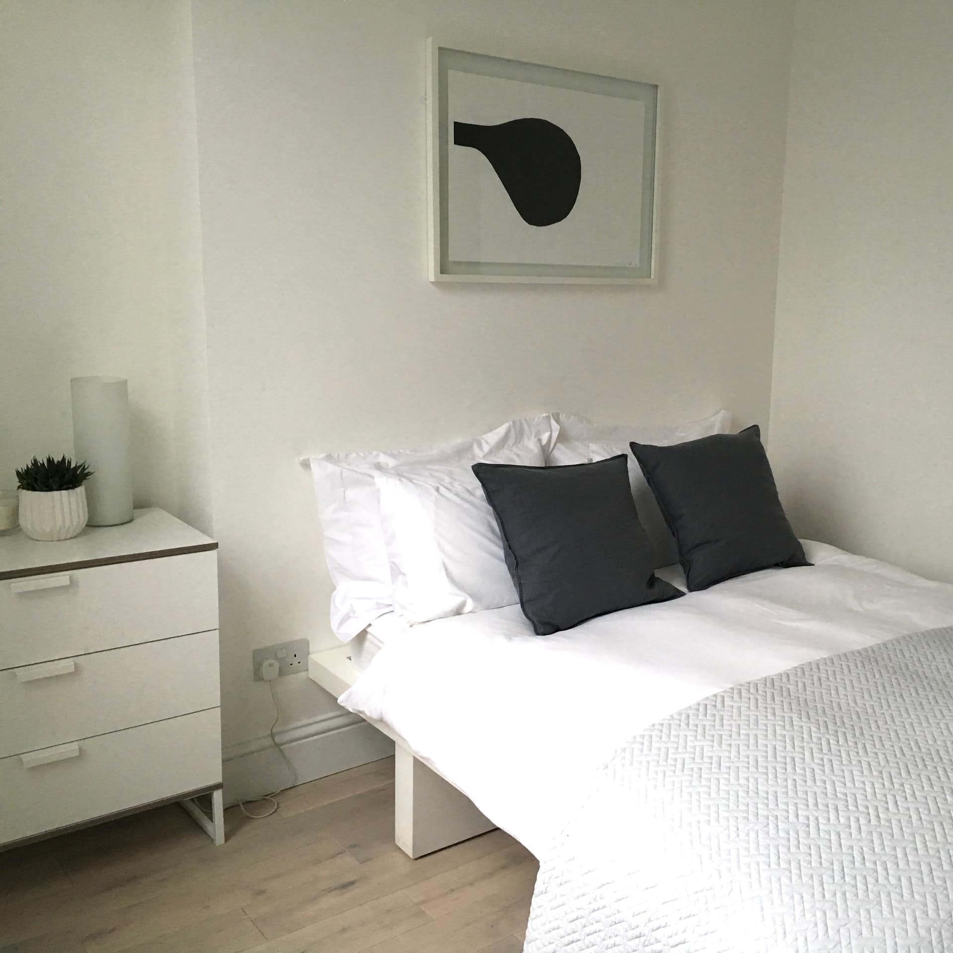A bedroom decorated in black and white decor with a queen size bed and white bedding and black pillows.