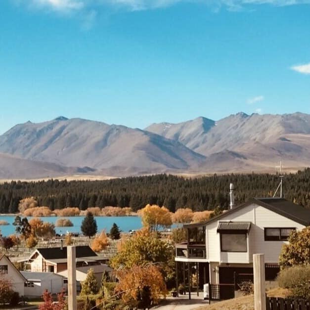 A view of Lake Tekapo and mountains in the background with a neighbourhood in the foreground among evergreen trees