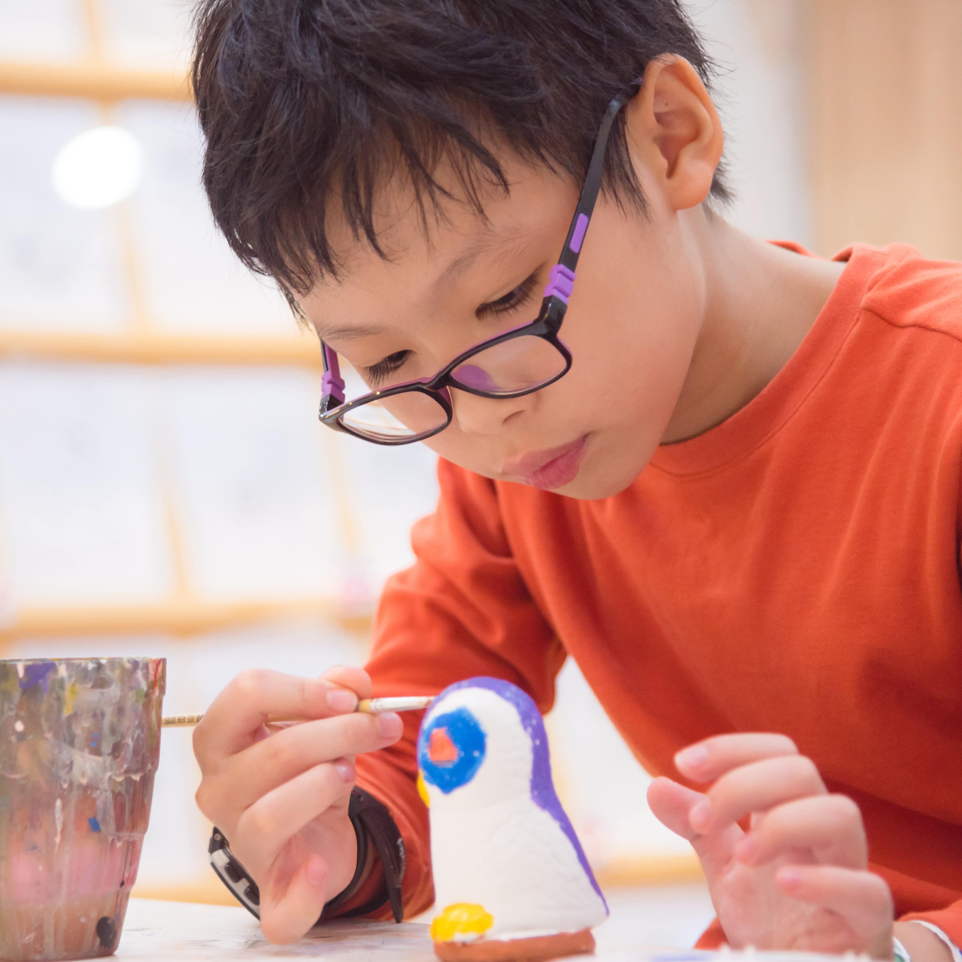 Young boy with glasses painting a ceramic object in a class