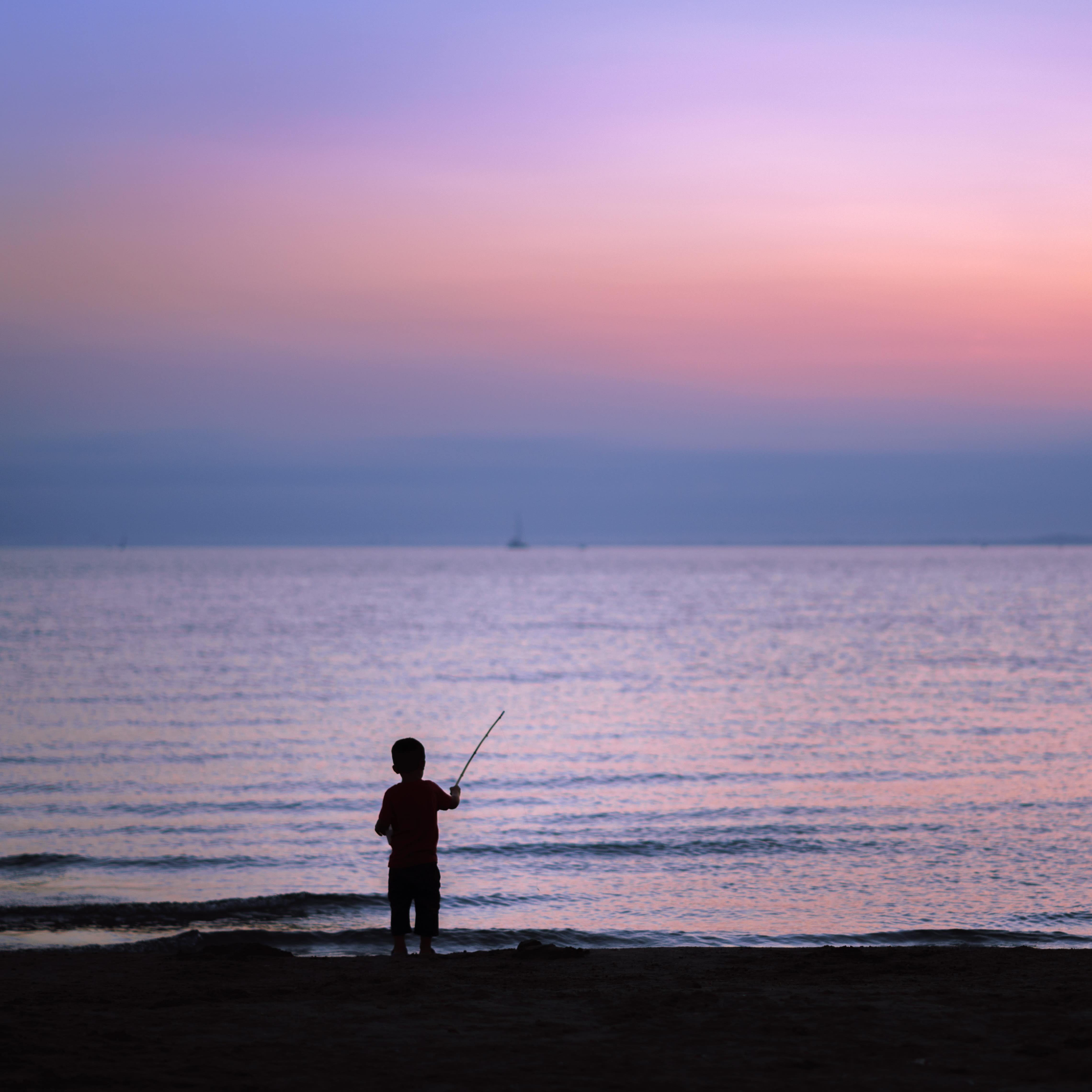 Silhouette of a child fishing on the shore of a beach at sunset