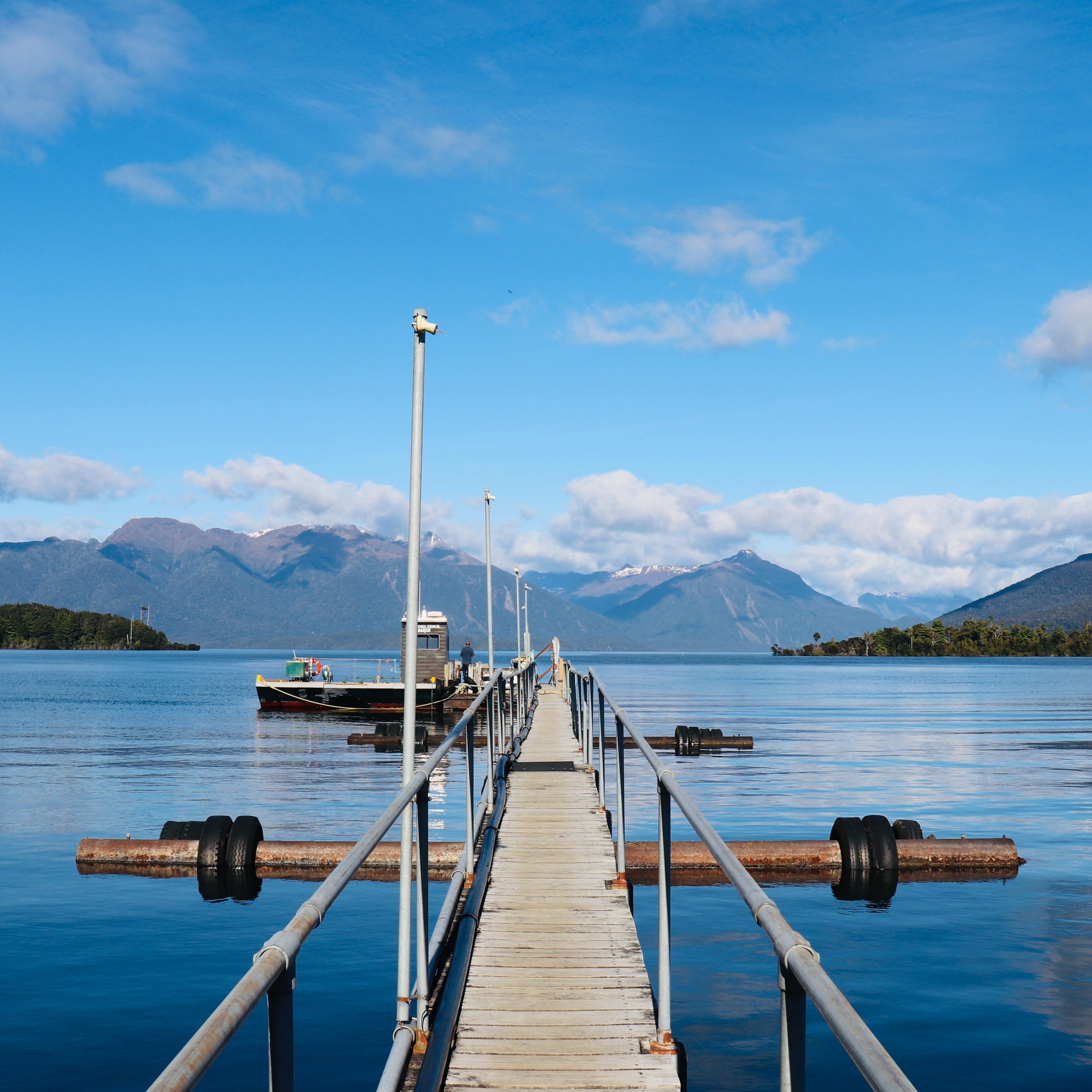 A narrow dock crossing the blue waters of Lake Te Anau with mountains in the background