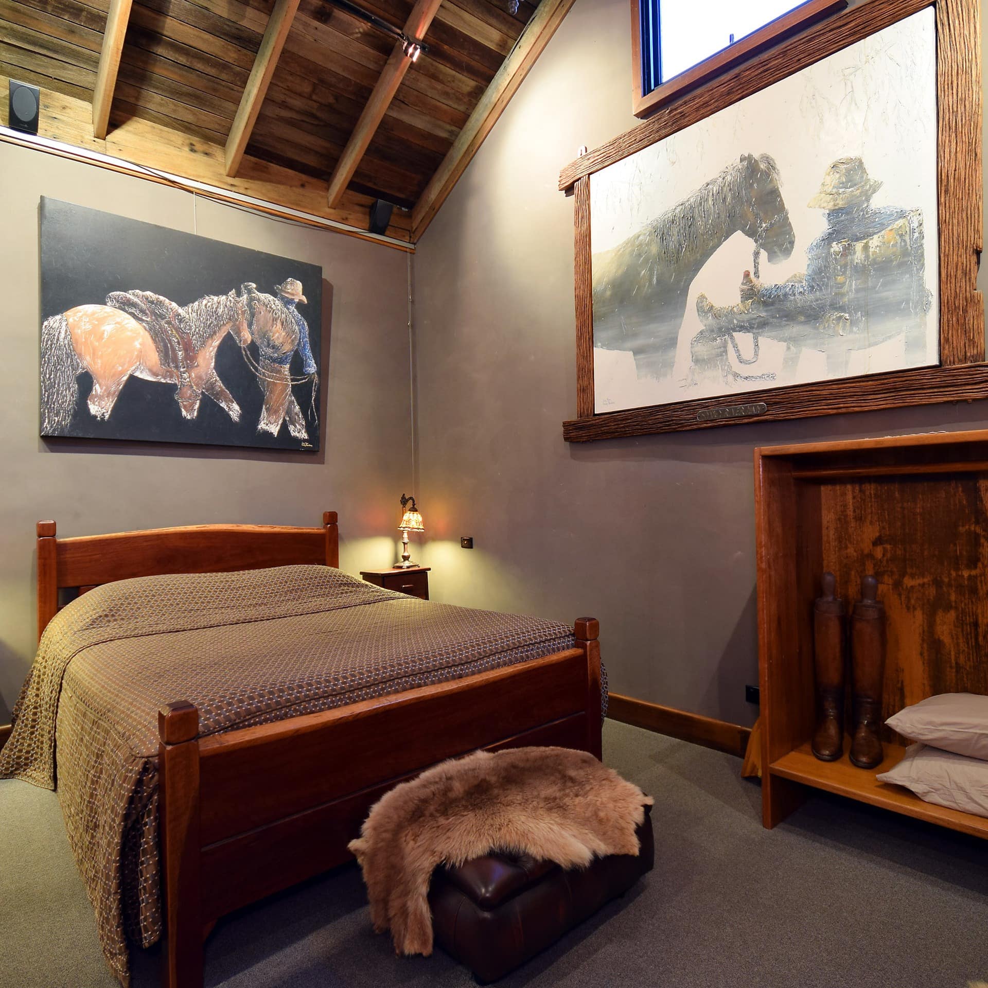 Spacious, rustic bedroom with grey walls and carpeted floors, king size bed with wood bed frame, equestrian art and decor.