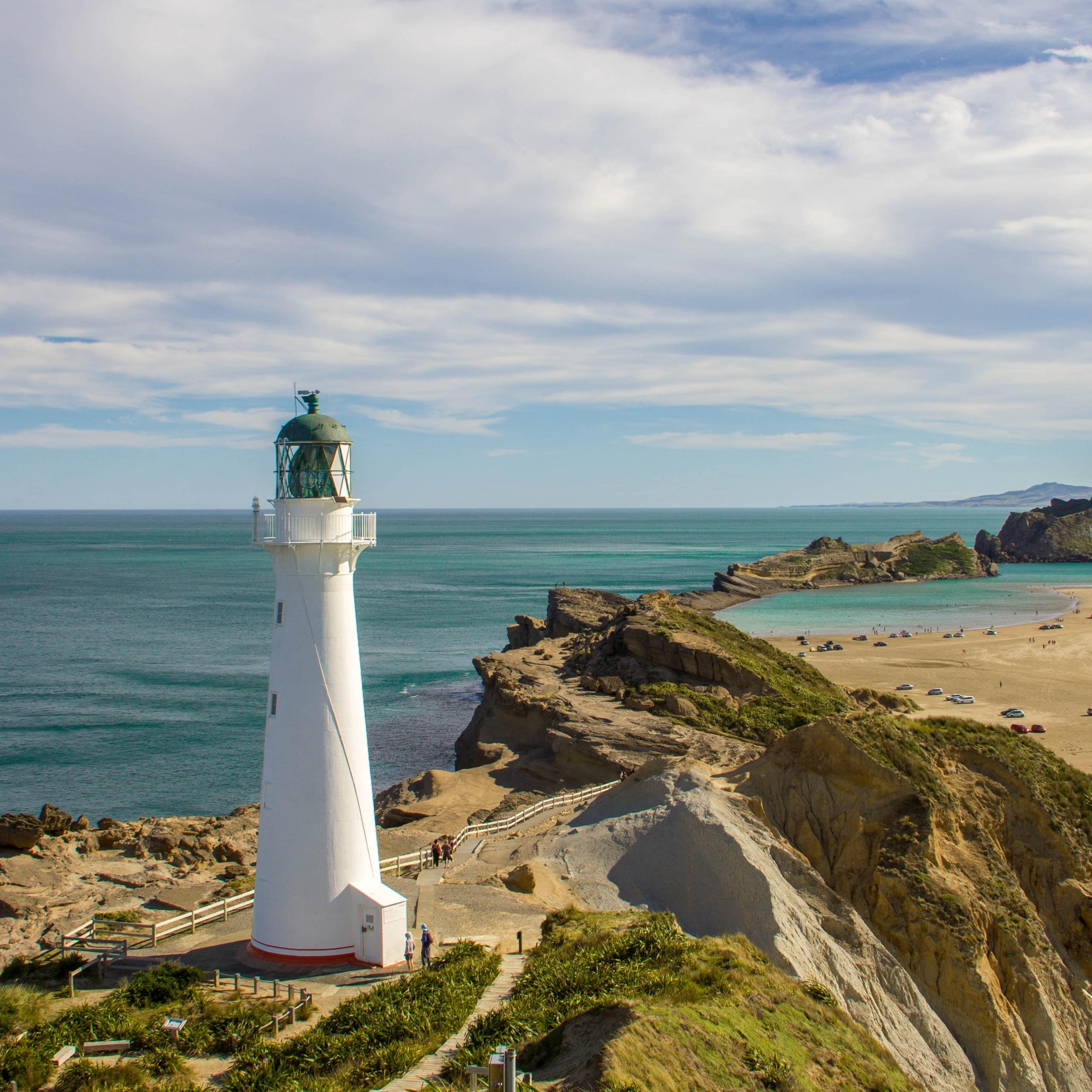 White lighthouse on Castlepoint Beach in Wairarapa, with the cliffs and ocean on each side