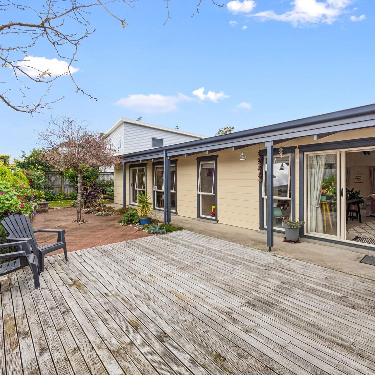 A cozy beach house with a wooden deck in the foreground surrounded by a small garden and other houses in the background