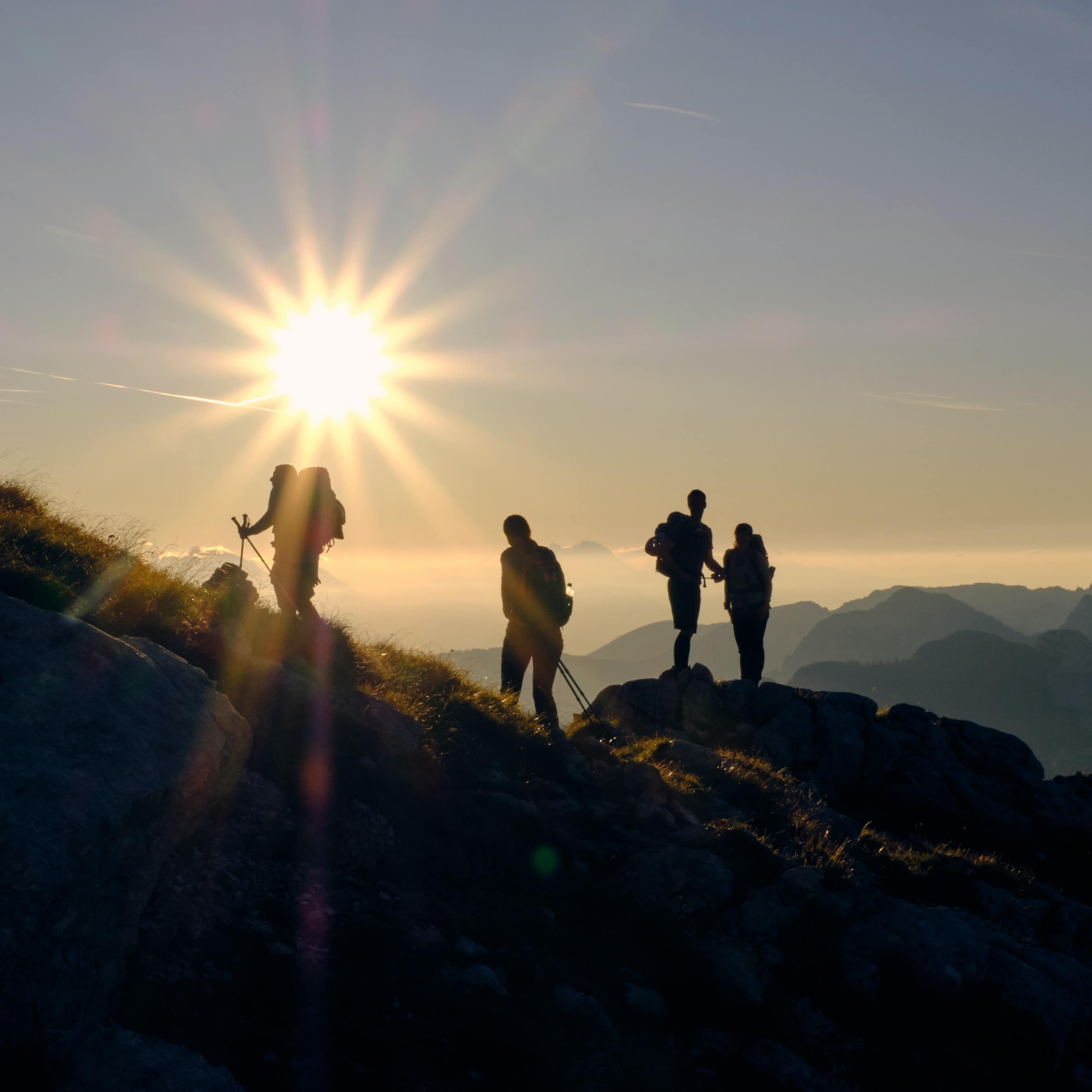 Silhouettes of four people hiking in the mountains with a large sun glare