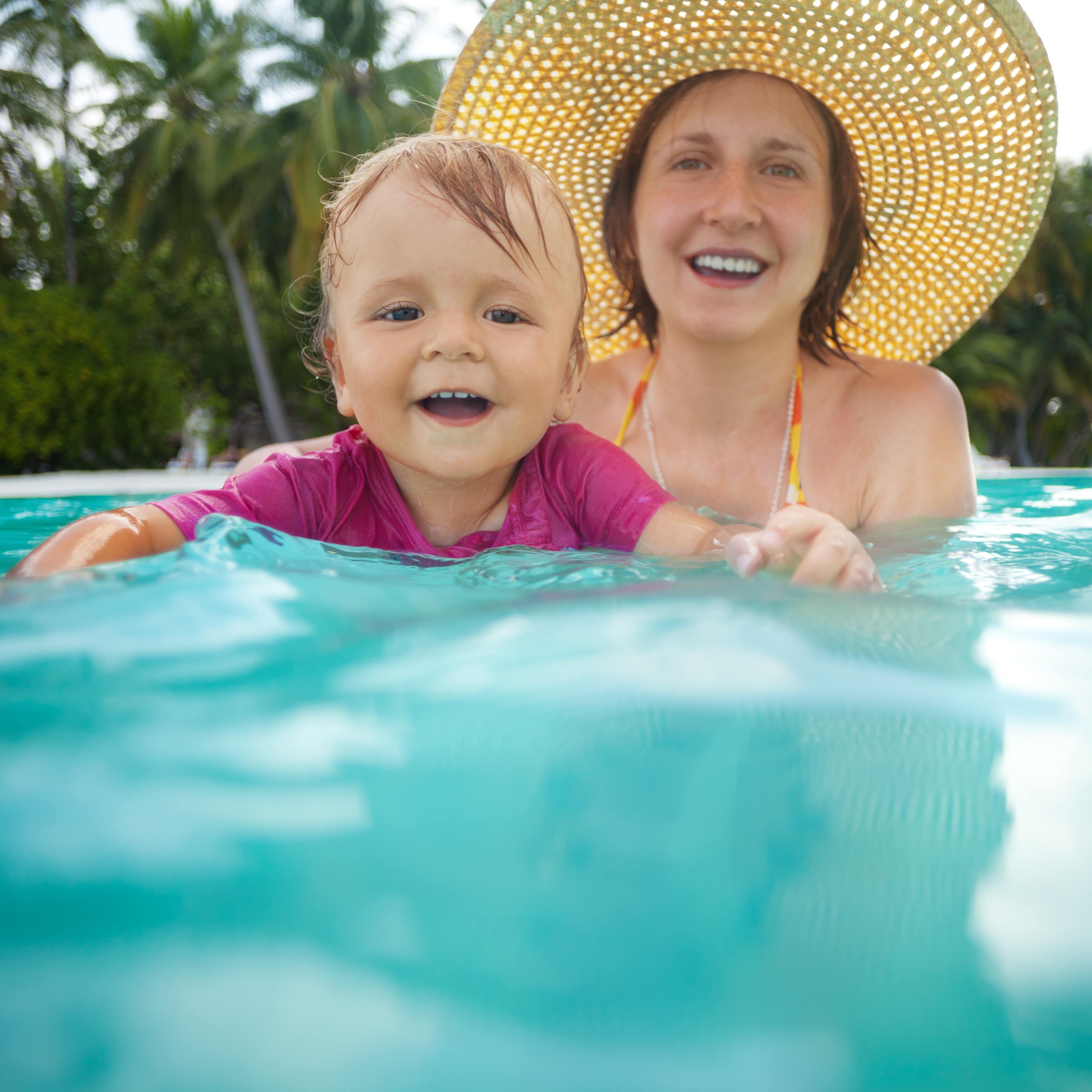 Mom with big sun hat on holding happy baby in tropical lagoon