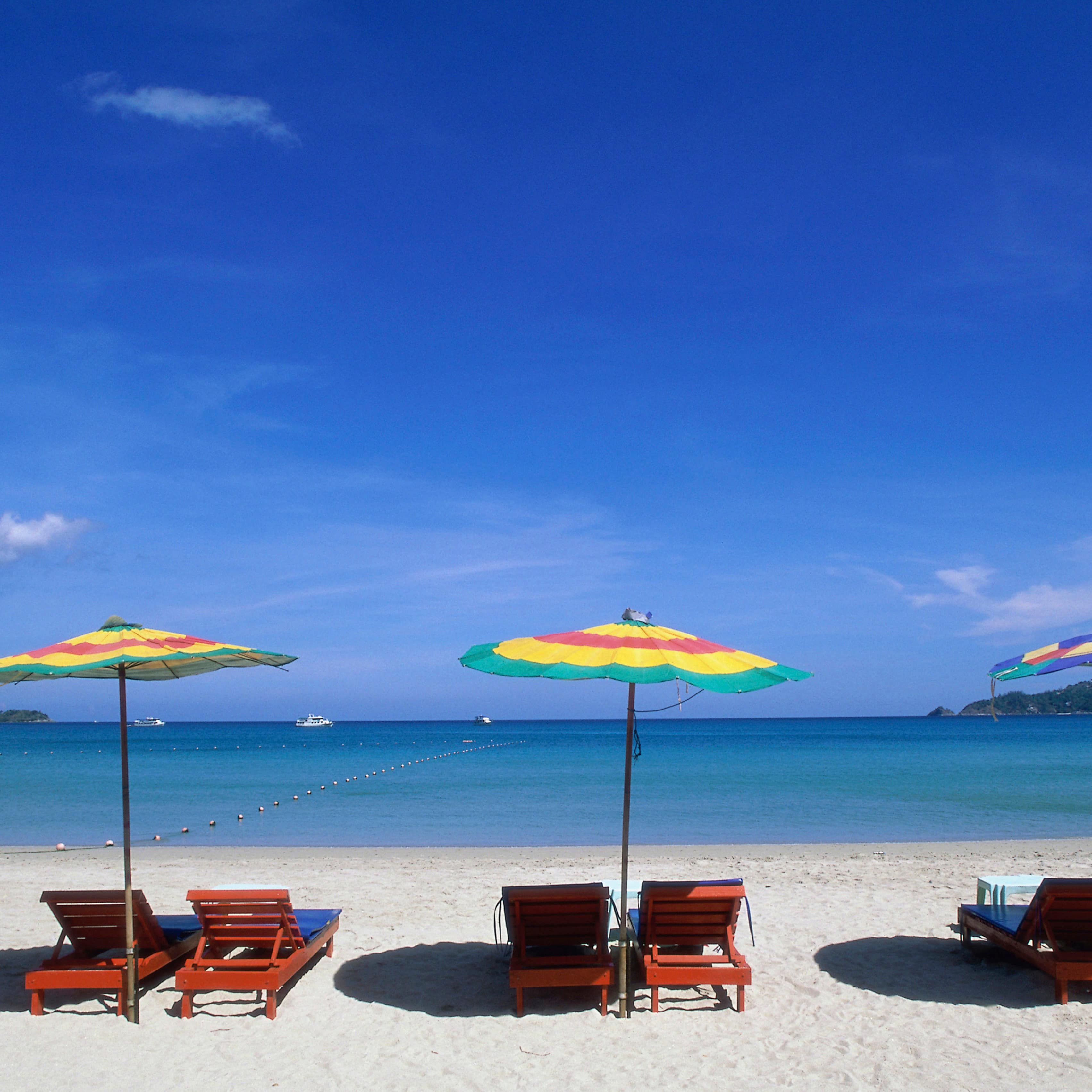 Colorful umbrellas above pairs of beach chairs looking out on the blue waters of Phuket