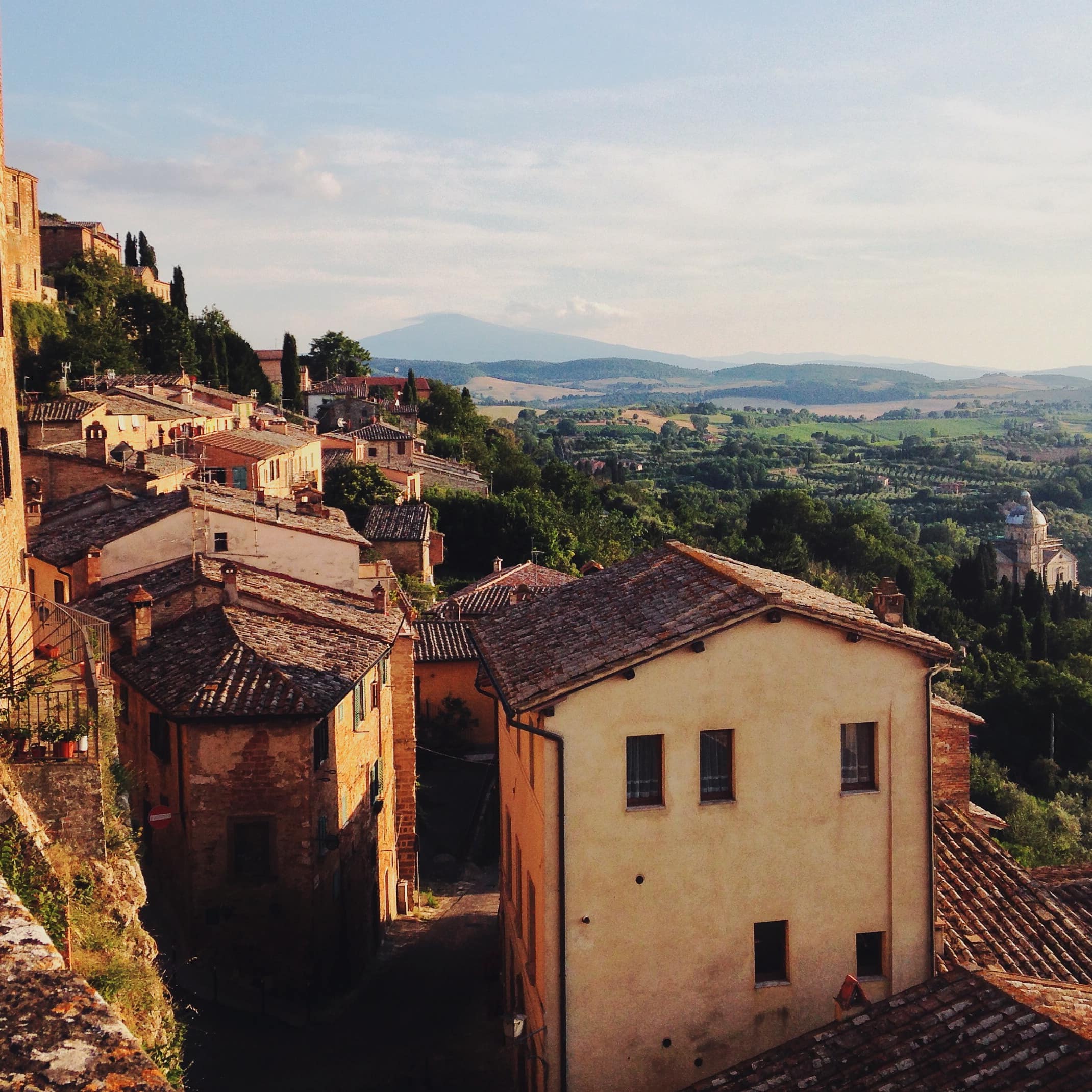 An Italian village, Montepulciano, on a hillside overlooking a lush, green valley with another mountain in the background