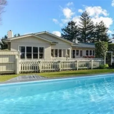 View of a backyard of a family holiday home with a swimming pool in the foreground on a bright day