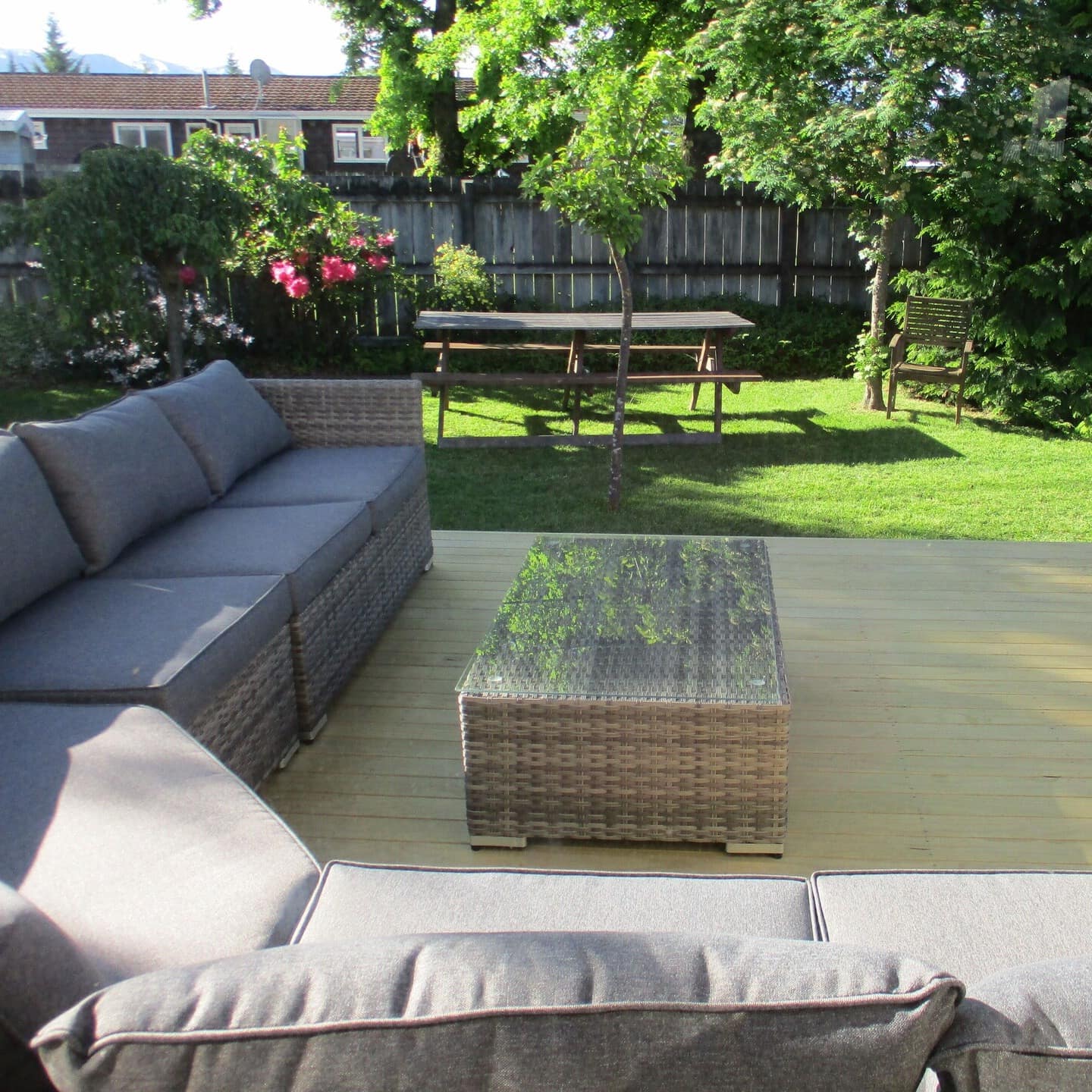 The fenced backyard of a holiday home with a wrap-around couch on the wooden patio