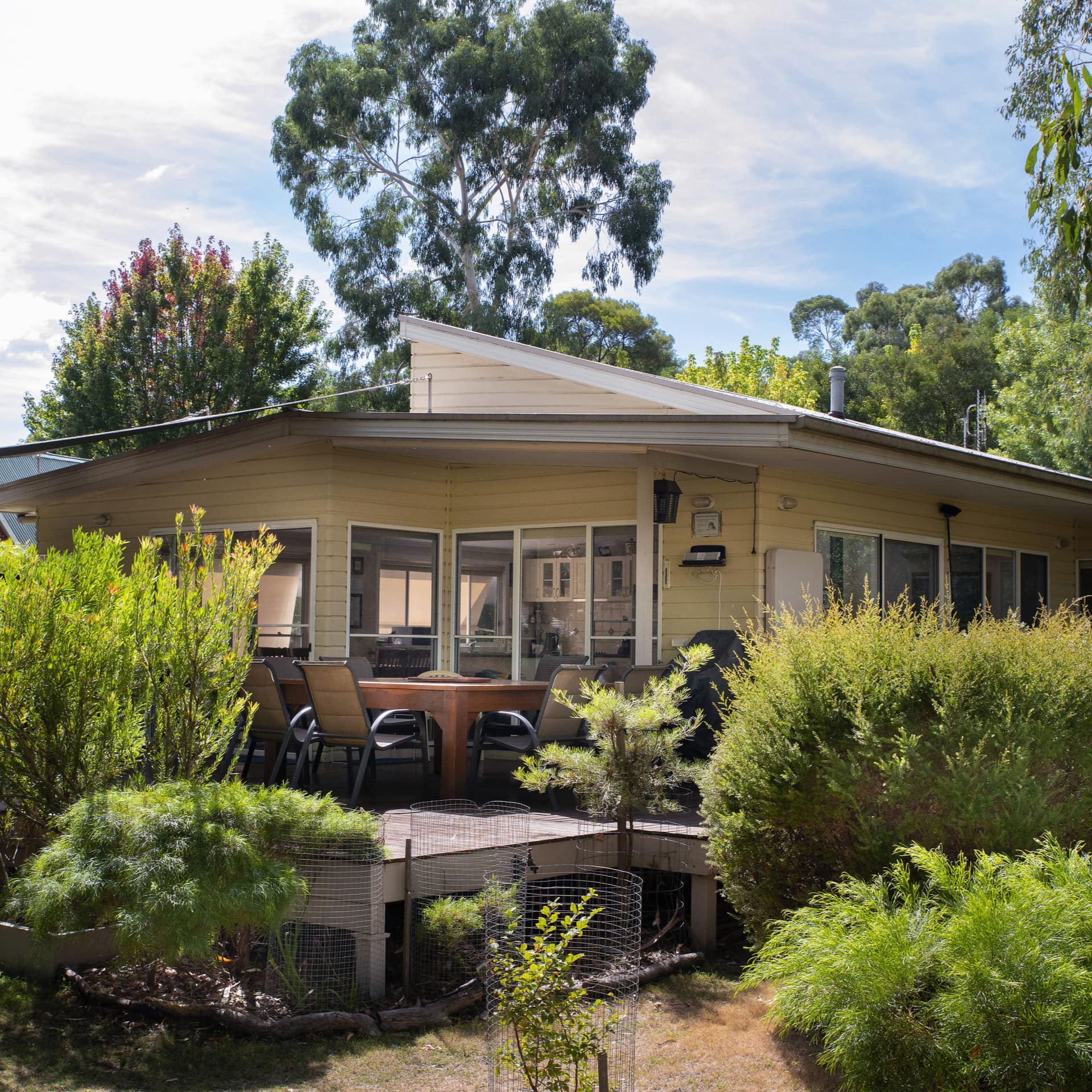 A modern yellow cottage with a wooden deck and lush garden.