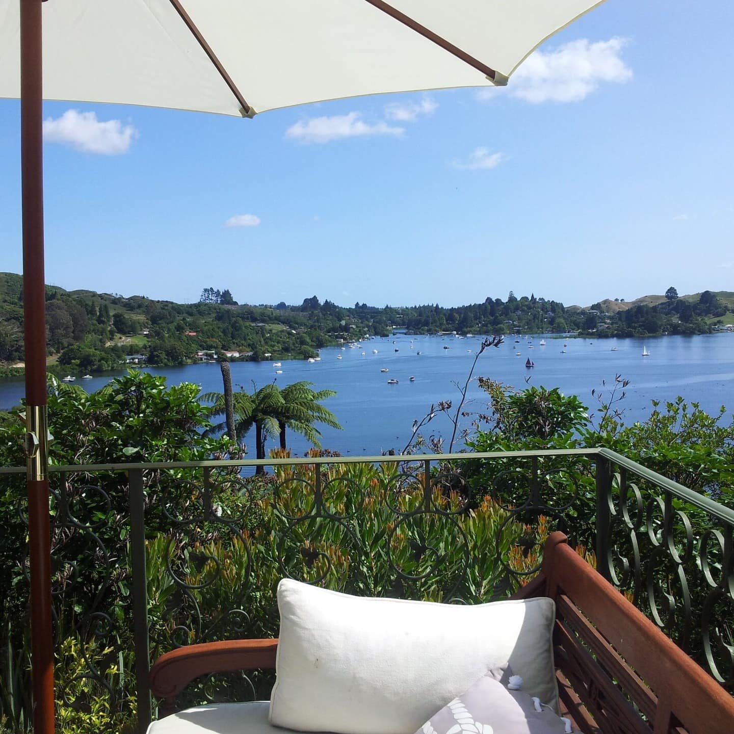 View of the blue lake dotted with boats from the balcony of a holiday home with a chair and umbrella in the foreground