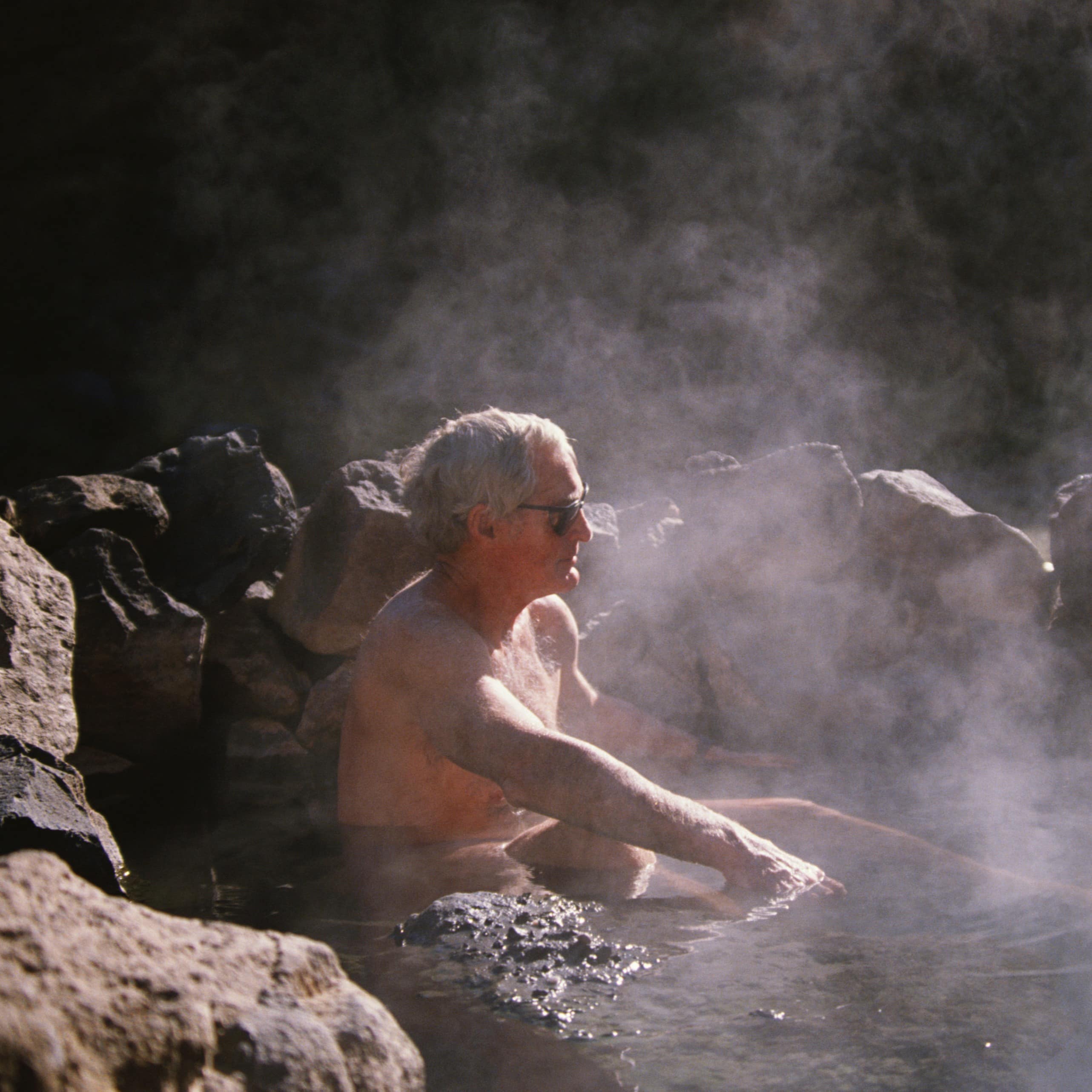 A man relaxing in a hot pool on a sunny day.