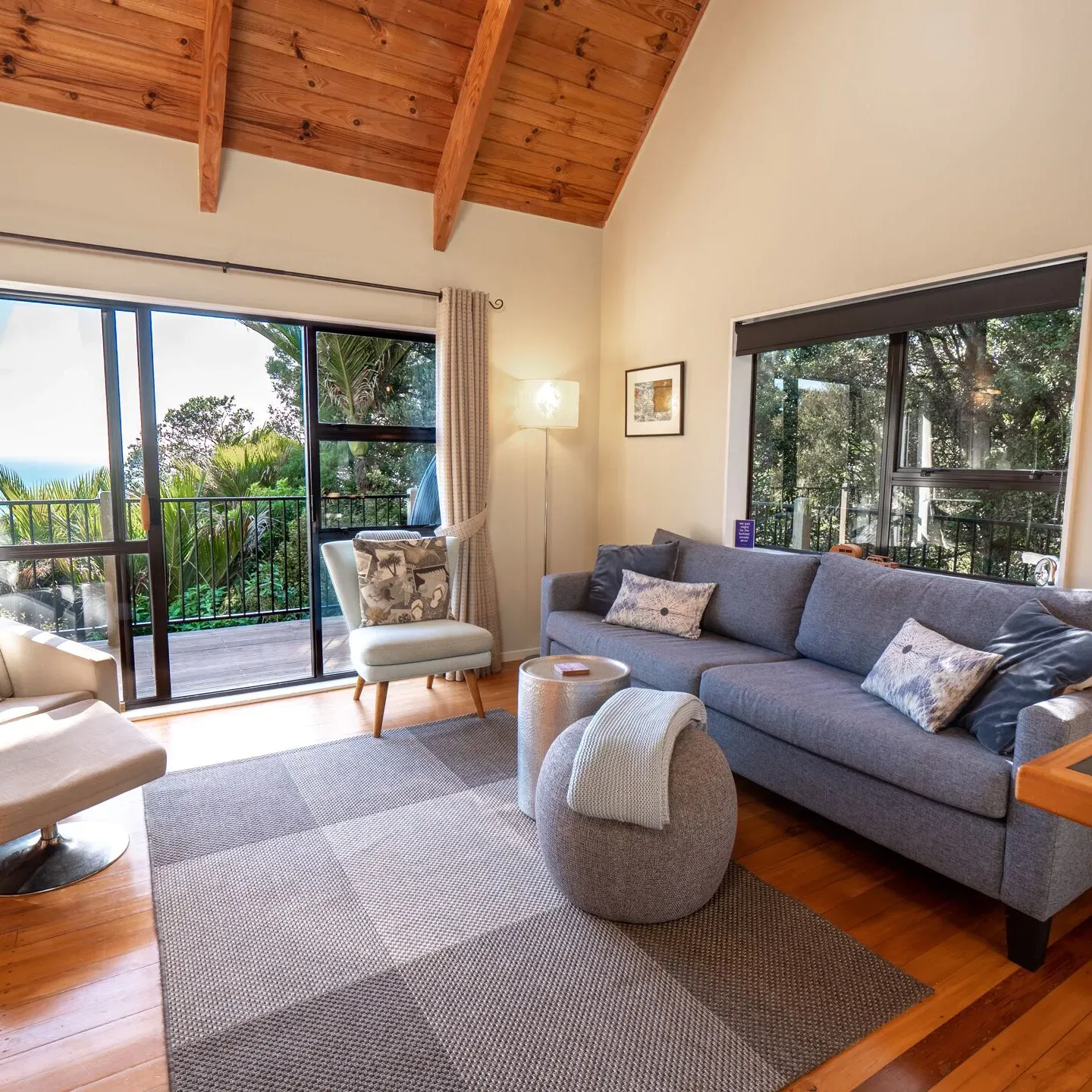 A cozy living room of a holiday home with couches and chairs and a window looking out on the palm trees and ocean