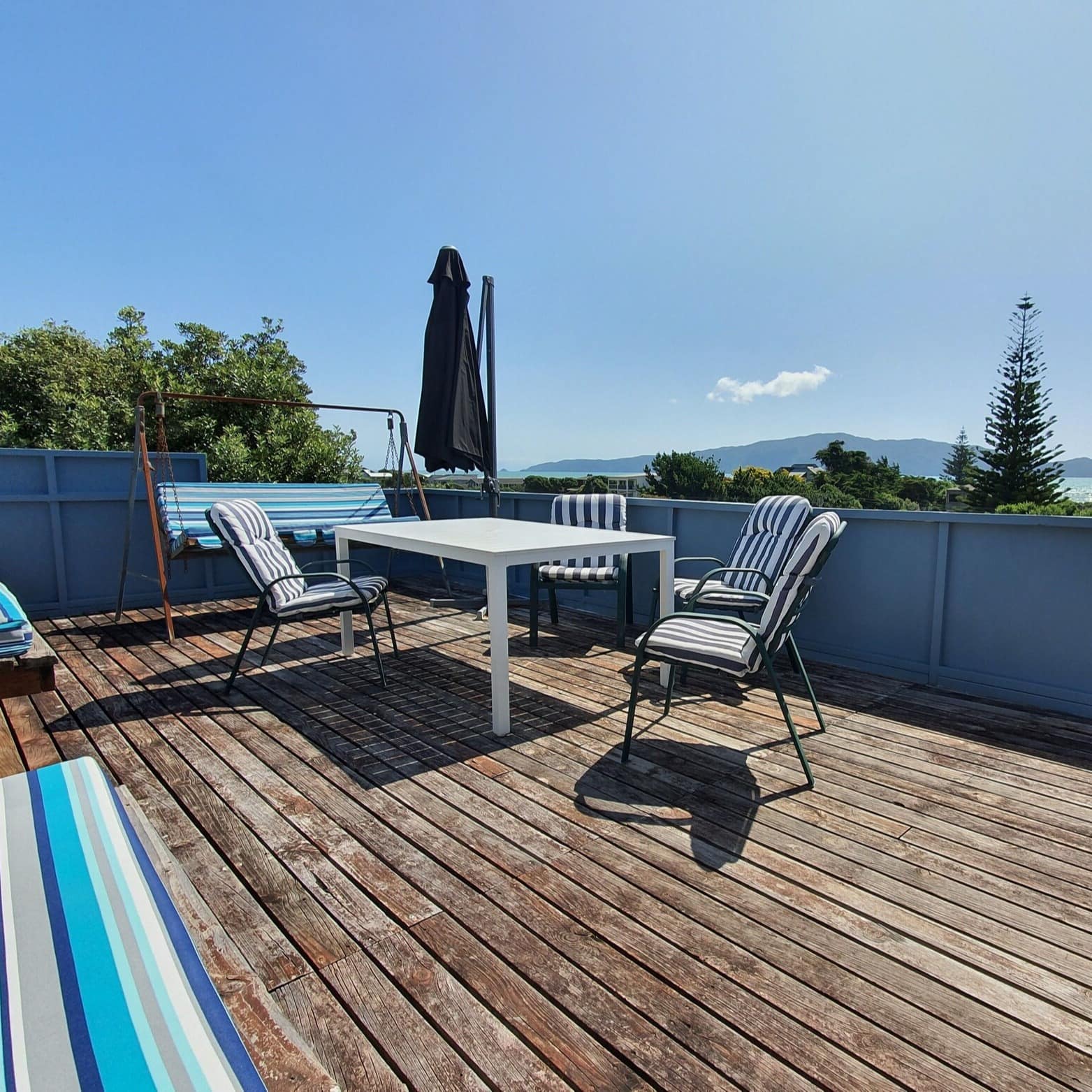 Back deck of a beach house set with a table and various chairs with the waters of Kapiti Coast in the background