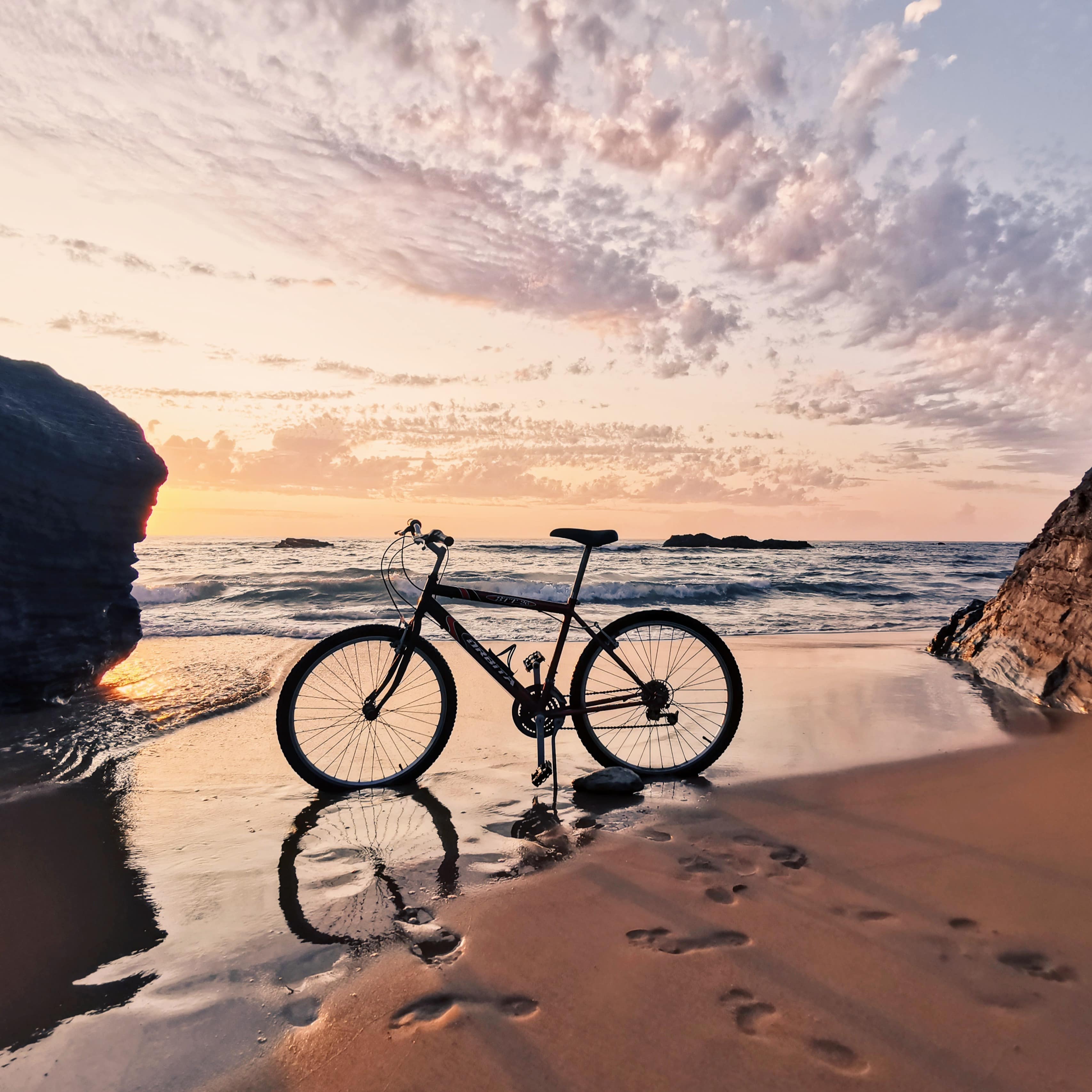 Black bicycle in the sand between two large rocks on the shore of a beach at sunset