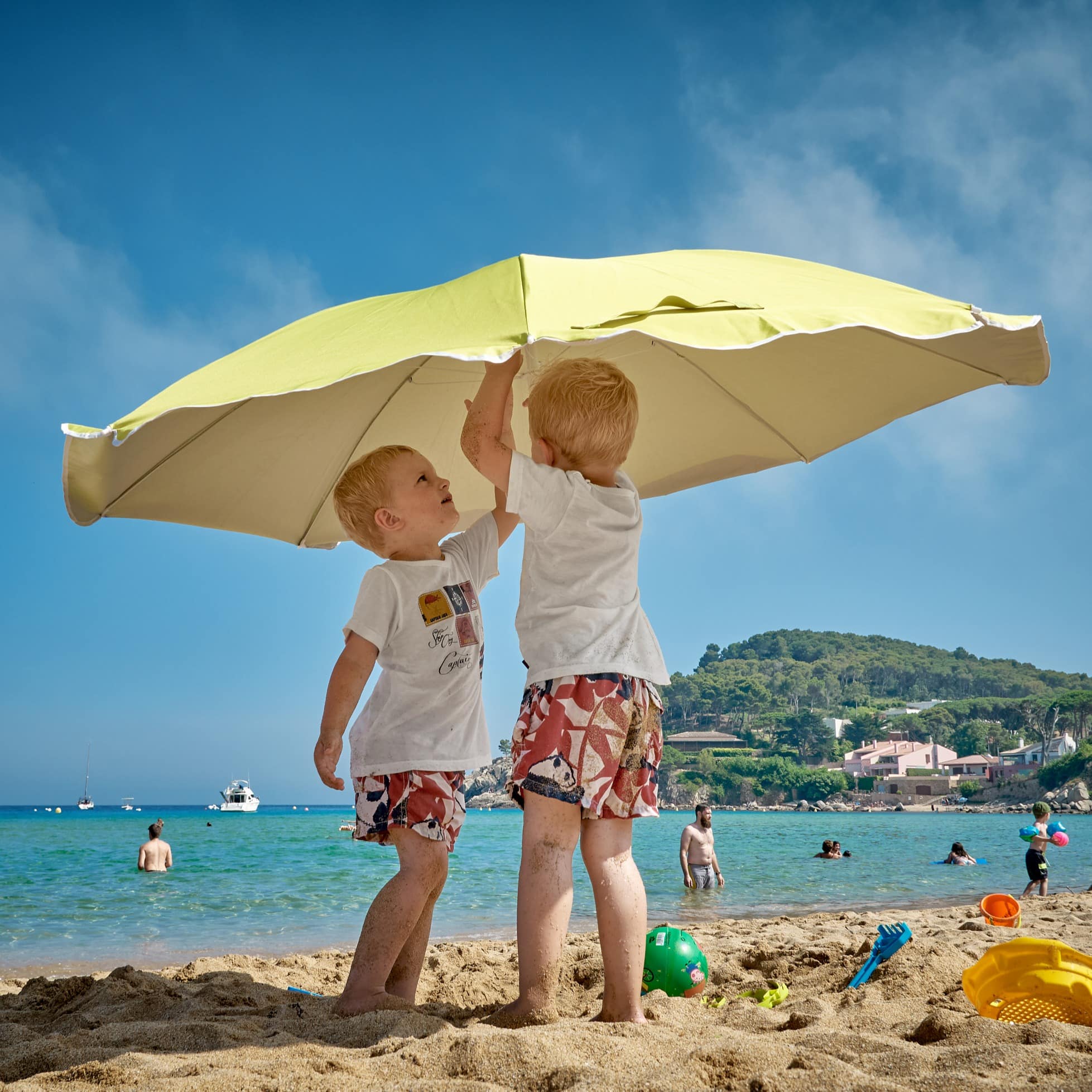 Two little boys setting up an umbrella on the beach.