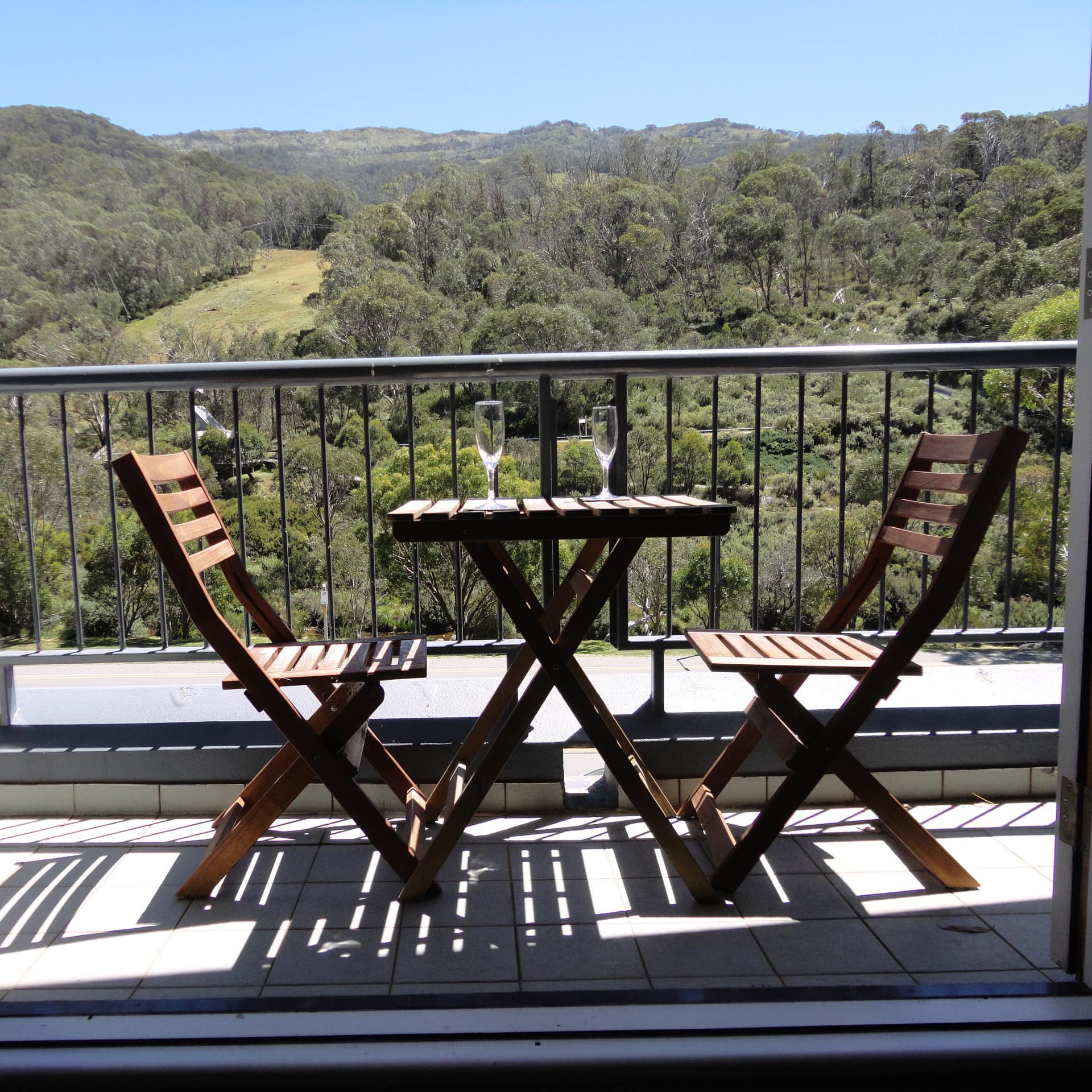 A balcony with expansive mountain views and a wooden dining set with champagne glasses.