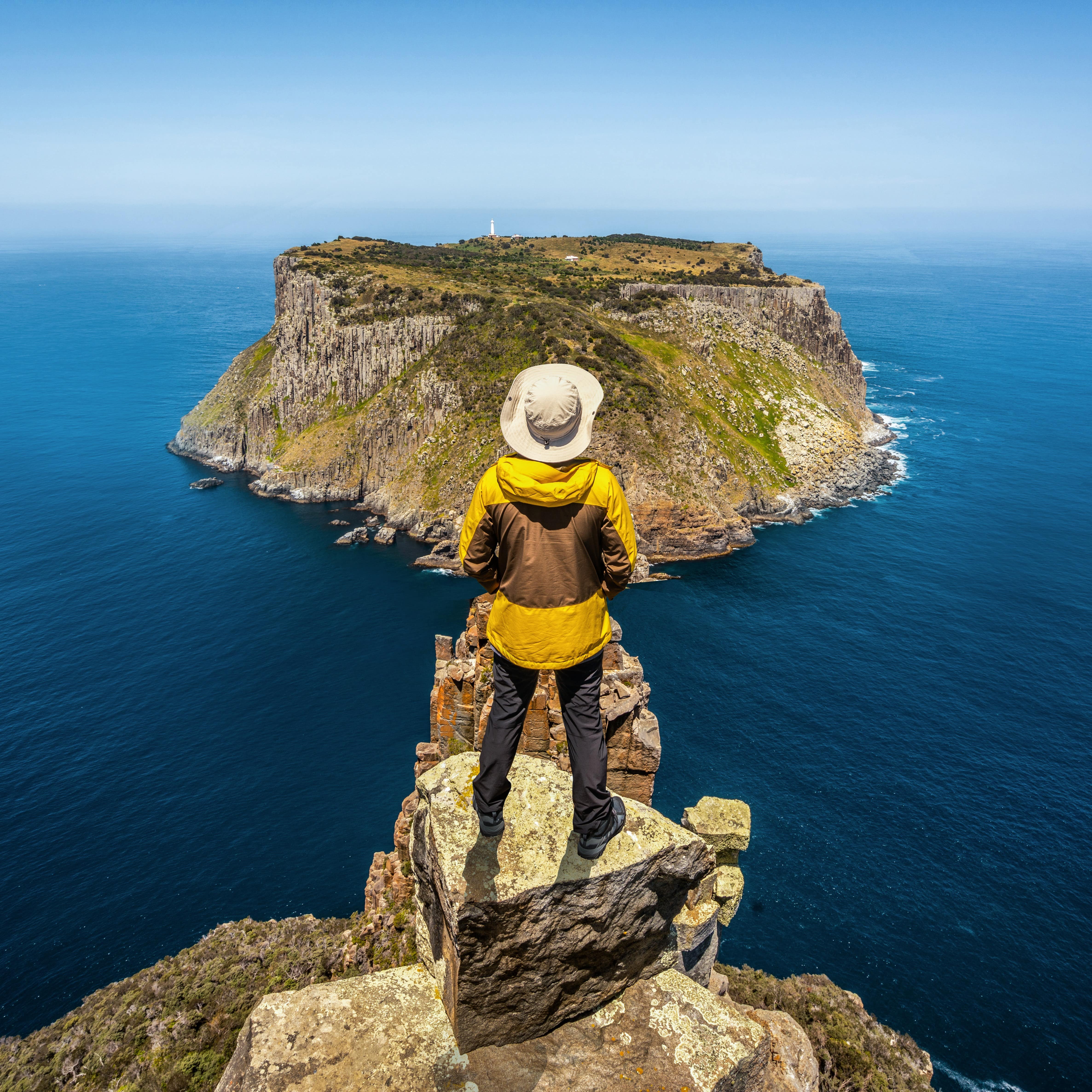 A young man hiking on the cliffs of an island near Abel Tasman National Park, with deep blue water on each side
