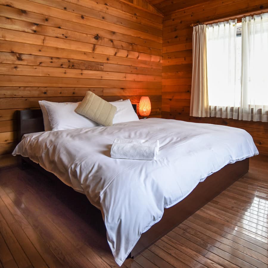 Spacious bedroom with hardwood floors, wood-panelled walls, a king size bed, white bedding, and a wide window.
