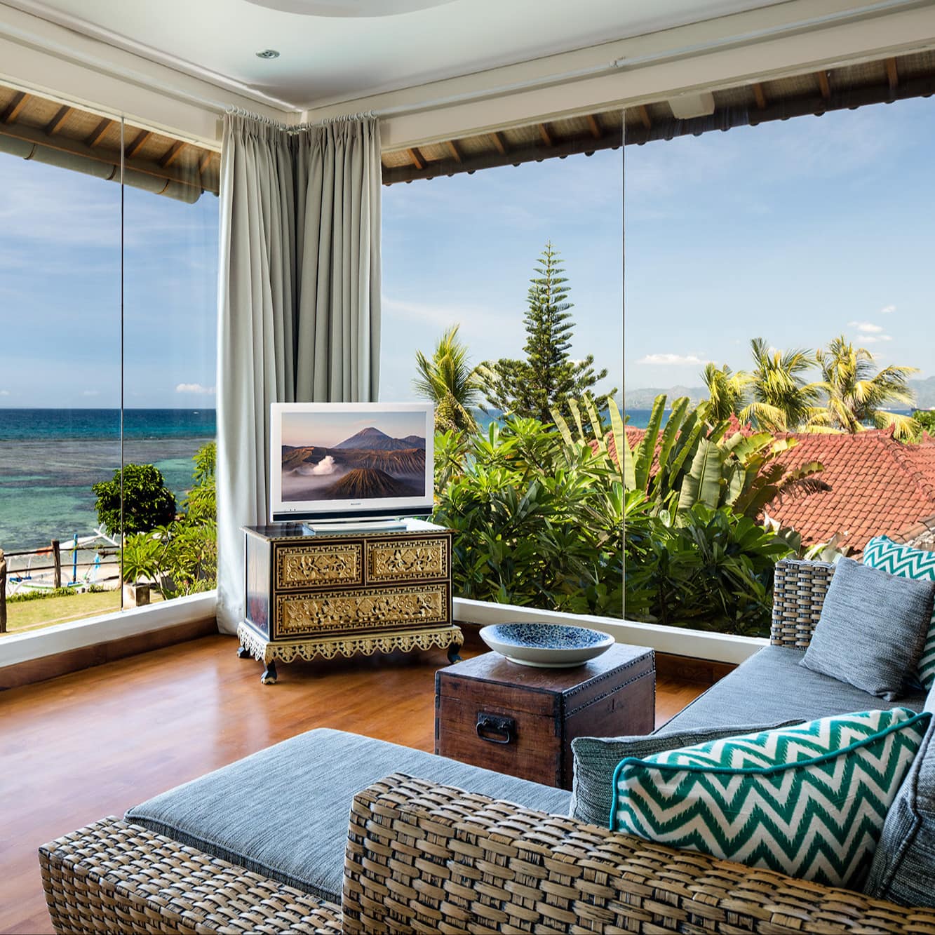 Living room with hardwood floors, wicker sofa with blue cushions, and floor to ceiling windows with ocean views.