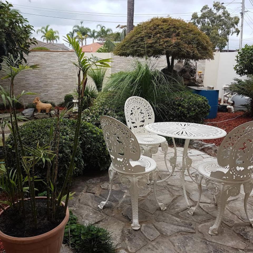 Flagstone patio with white, metal bistro dining set in a landscaped garden.