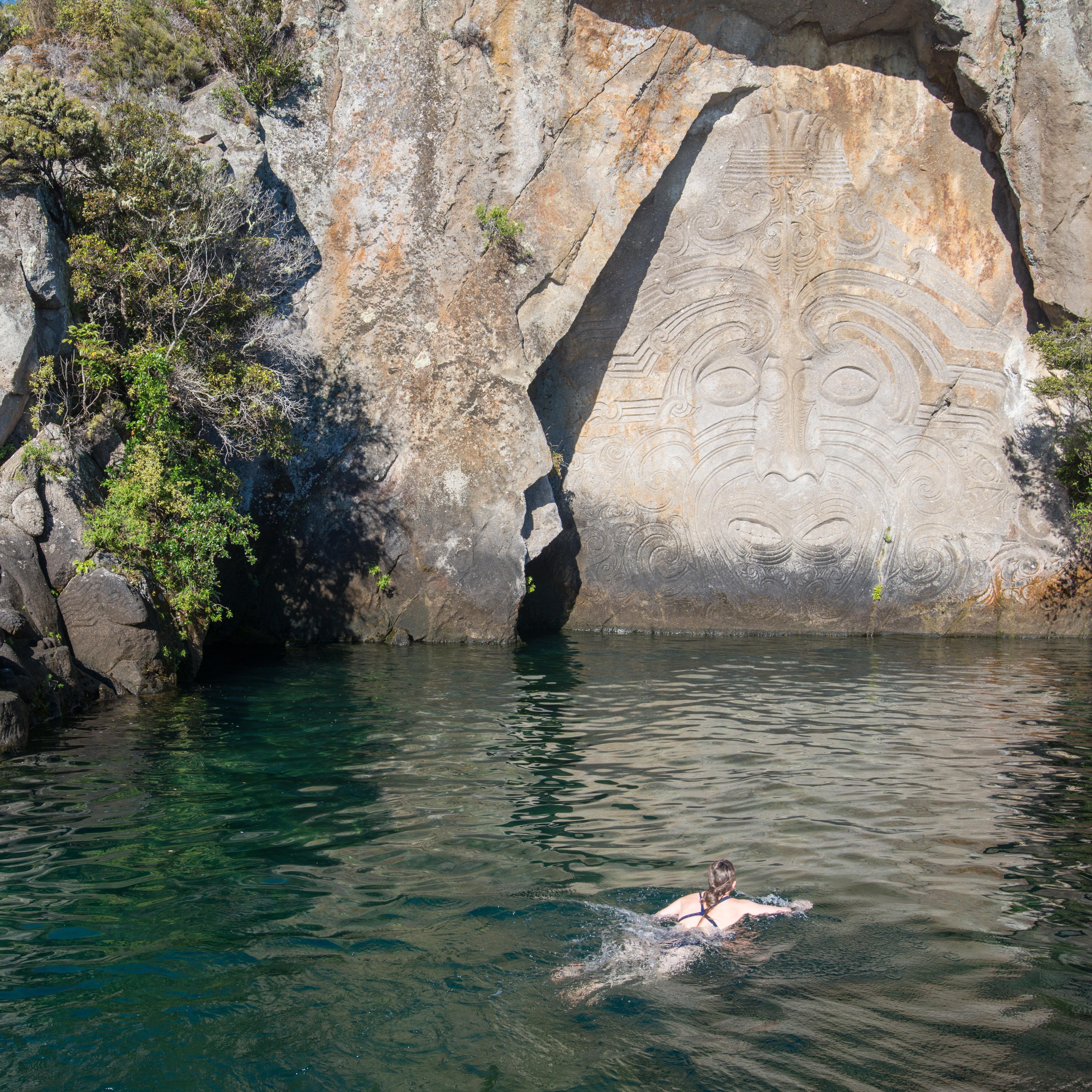 Tourist swimming in Lake Taupo with Maori rock carvings at the iconic tourist attraction place in Lake Taupo, New Zealand